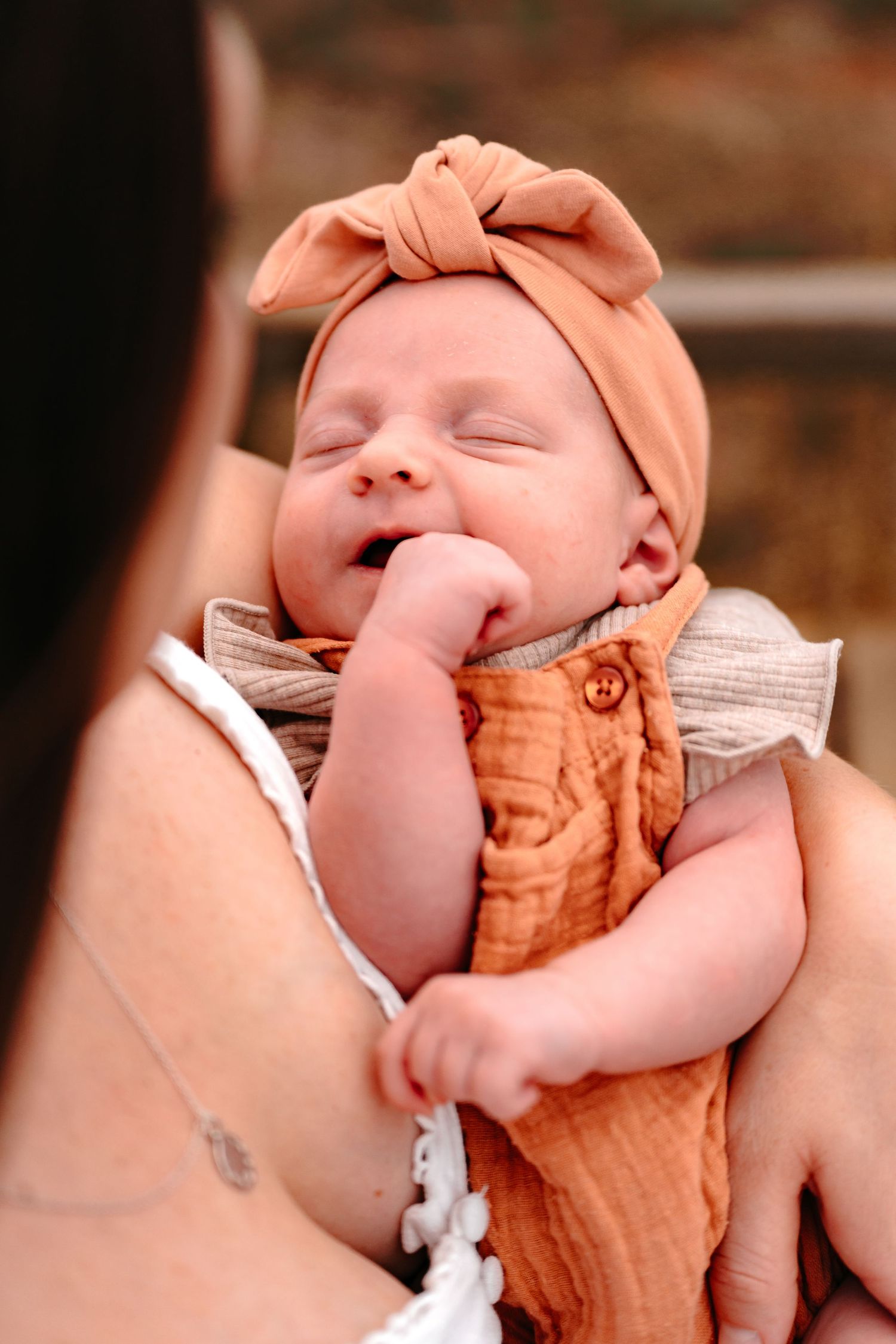 close up of a newborn baby who is sucking on their little hand. mother is looking down staring at the baby with adoration