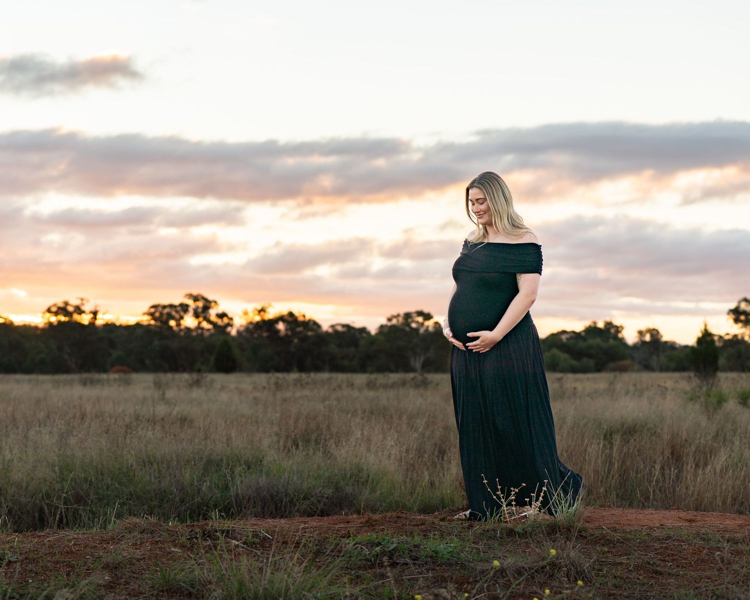 a pregnant mother walking and holding her little baby bump with a beautiful twilight, moody sunset in the background