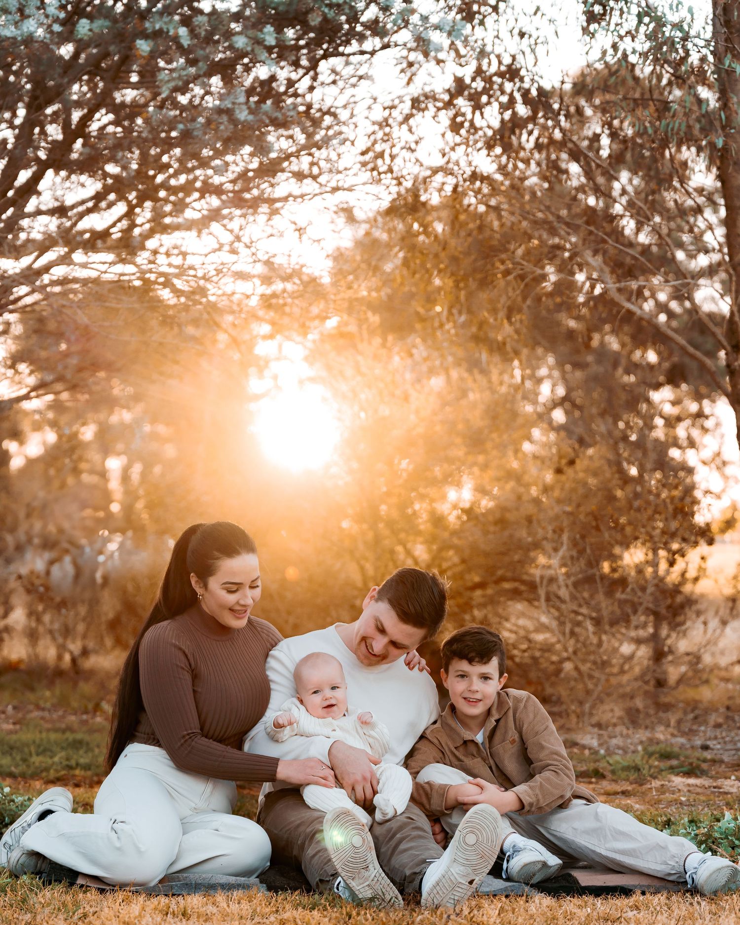 Family of 4. Mum, dad, baby & older borther. Authentic, relaxed moment of mum & dad admiring baby & the older brother smiling at the camera.