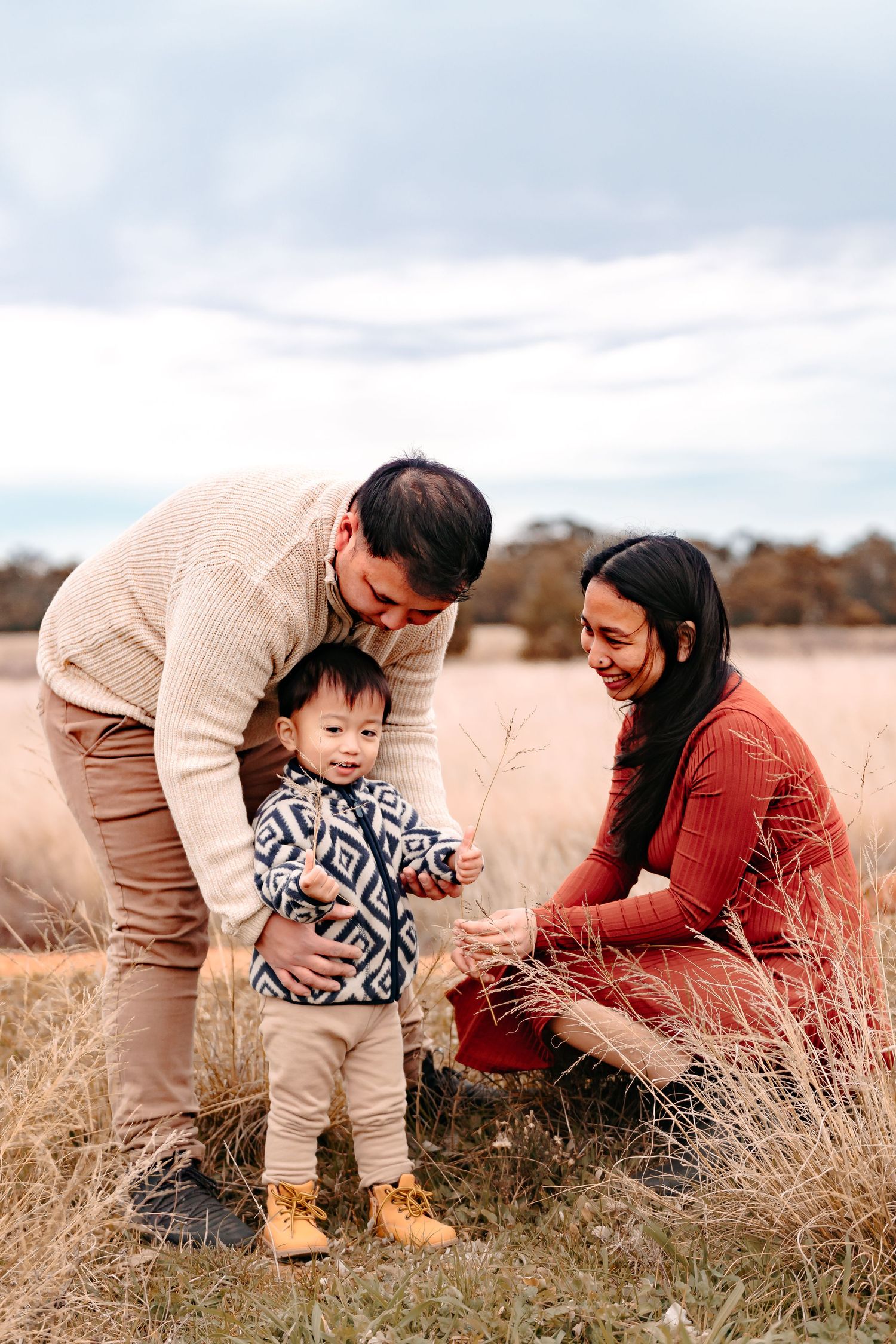 A mother & father playing with their 2 year old boy in a vast, open paddock.