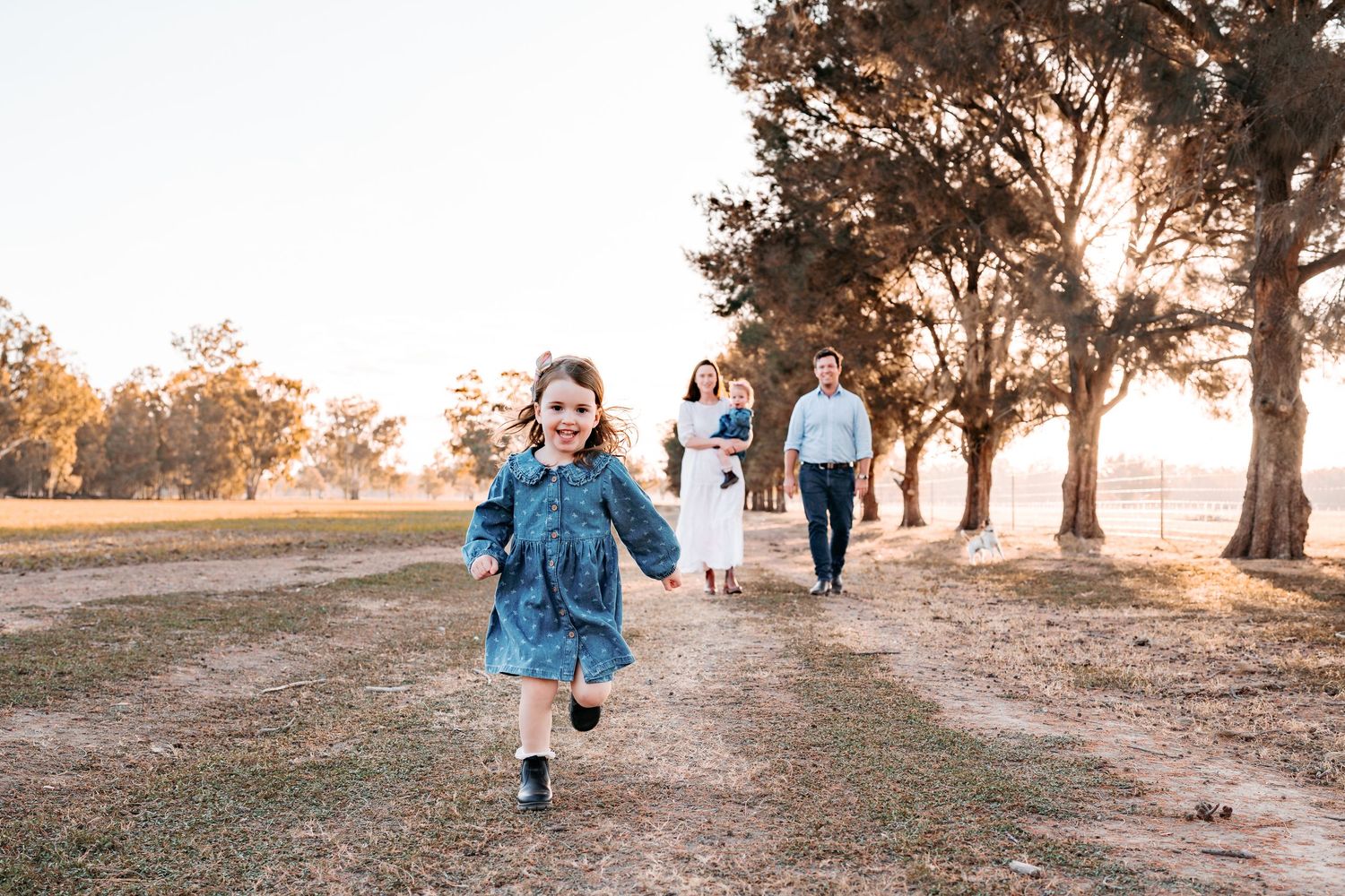 A FAMILY OF 4 IN A PADDOCK AND THE ELDEST DAUGHTER IS RUNNING AT THE CAMERA WHILST HER PARENTS LOOK ON IN ADMIRATION AND JOY