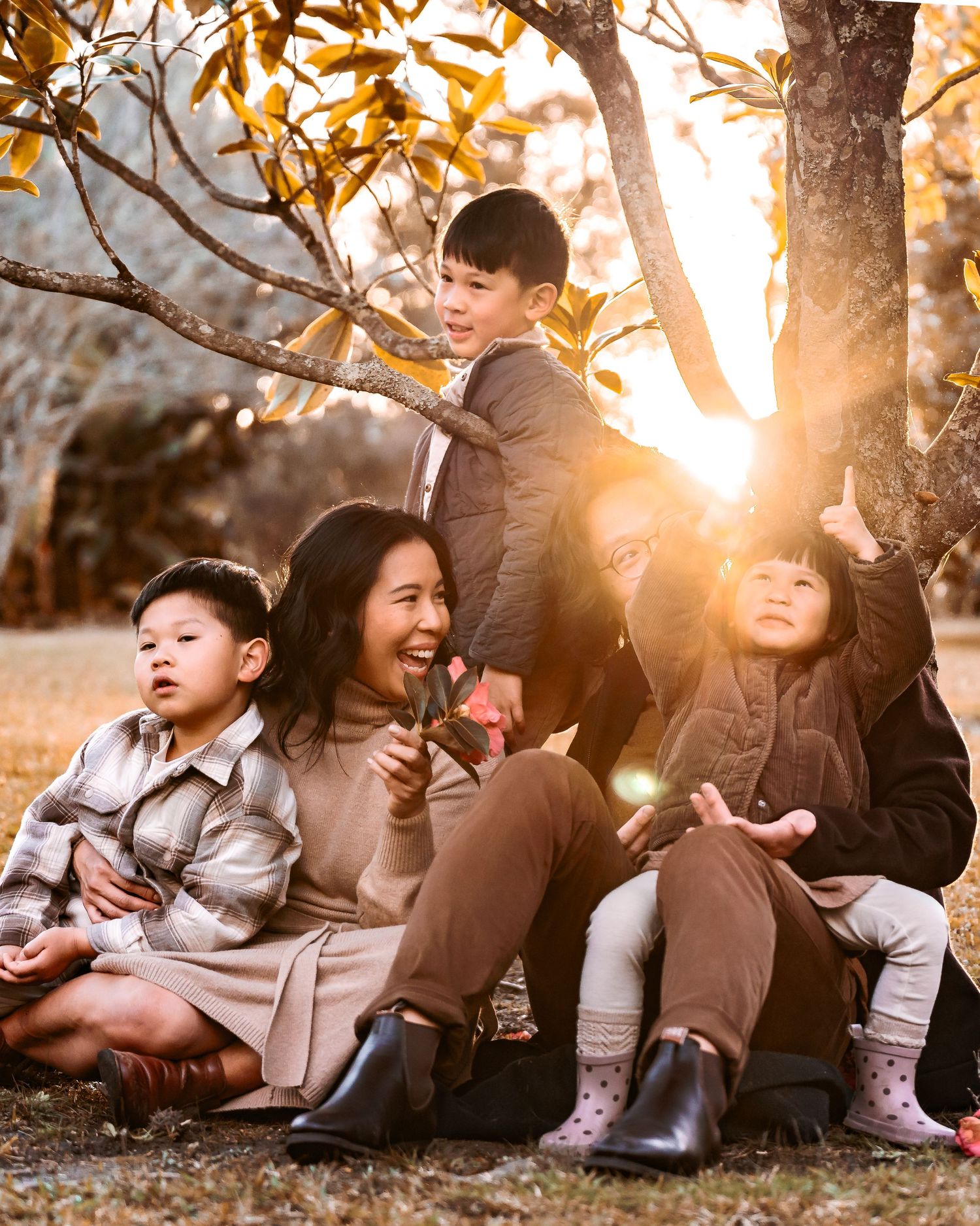 A beautiful family of 5 sitting & quietly connecting with a sun haze creeping through on the tree.
