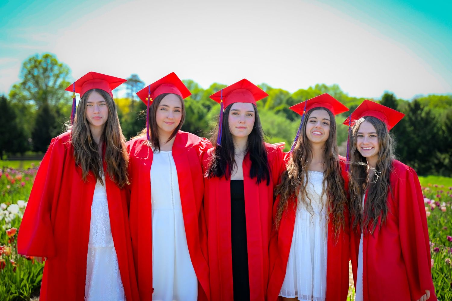 Group of graduates in red caps and gowns pose together in outdoor setting. Senior Photo.