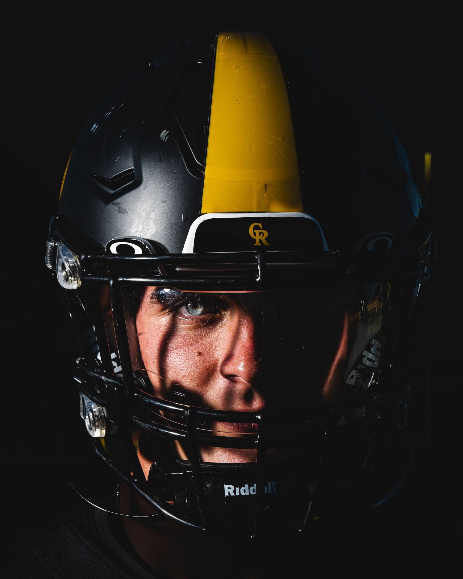Dramatic side profile of baseball player wearing black helmet with yellow accents. Senior Photo.
