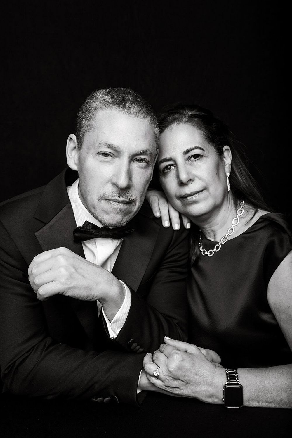 Affectionate black and white studio portraits of couple in formal wear against dark background.