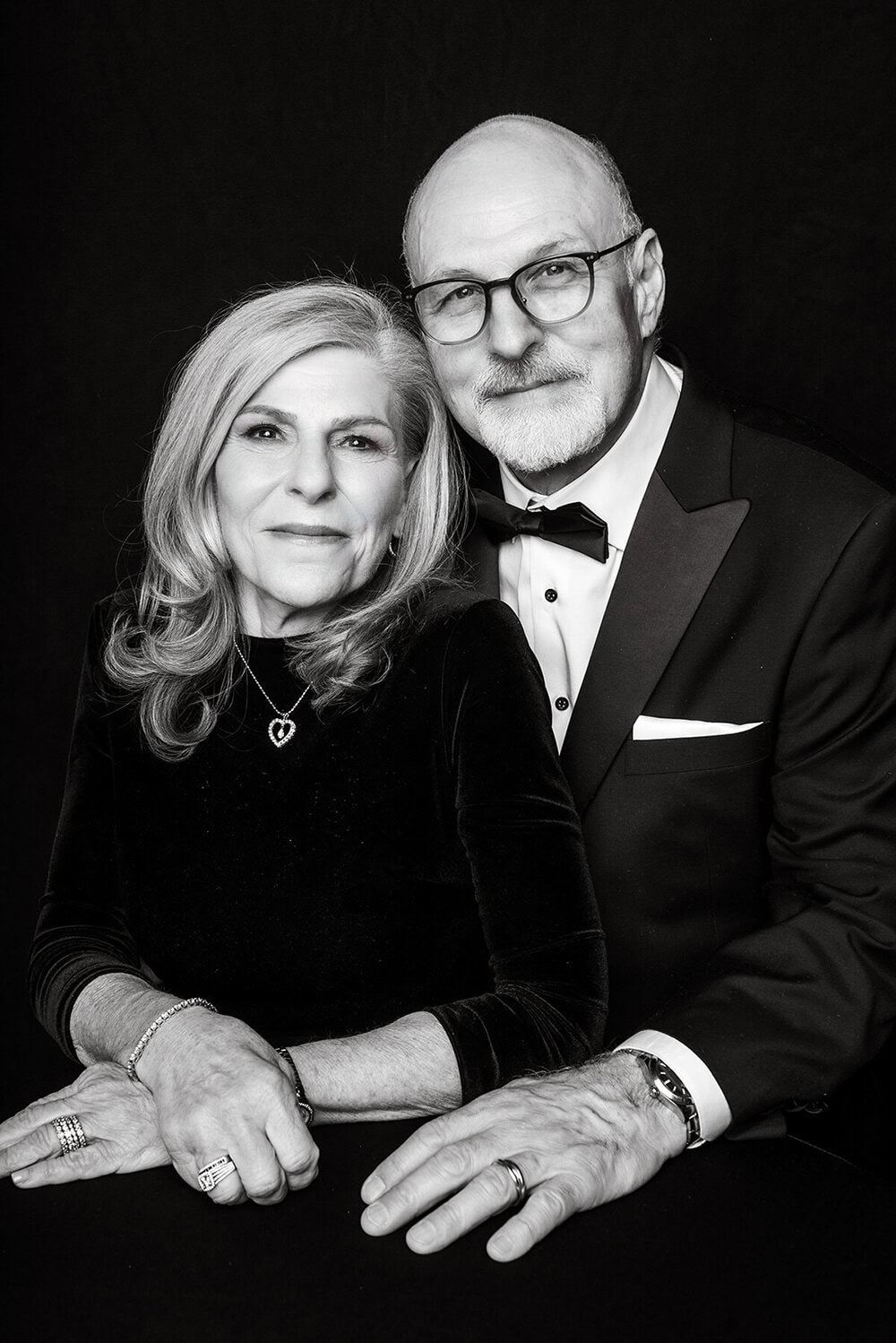 Elegant mature couple in formal black attire pose for intimate studio portrait series.