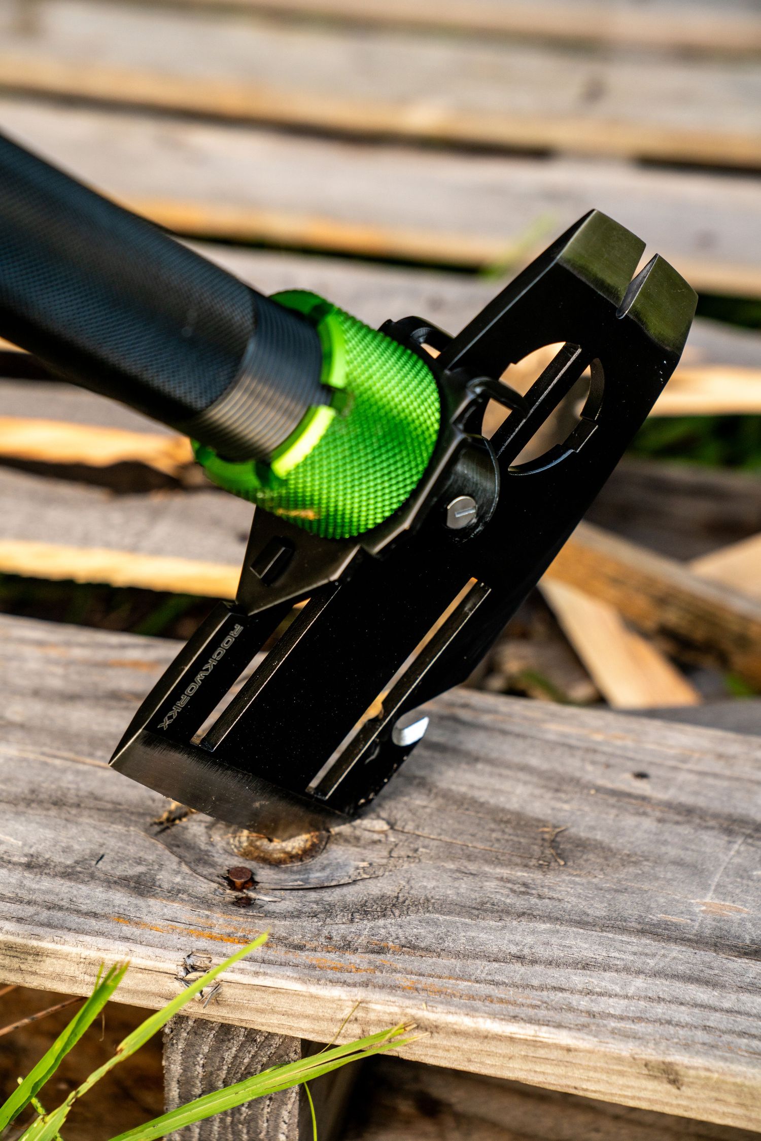 Black metal tool handle with green accent photographed on weathered wooden surface.