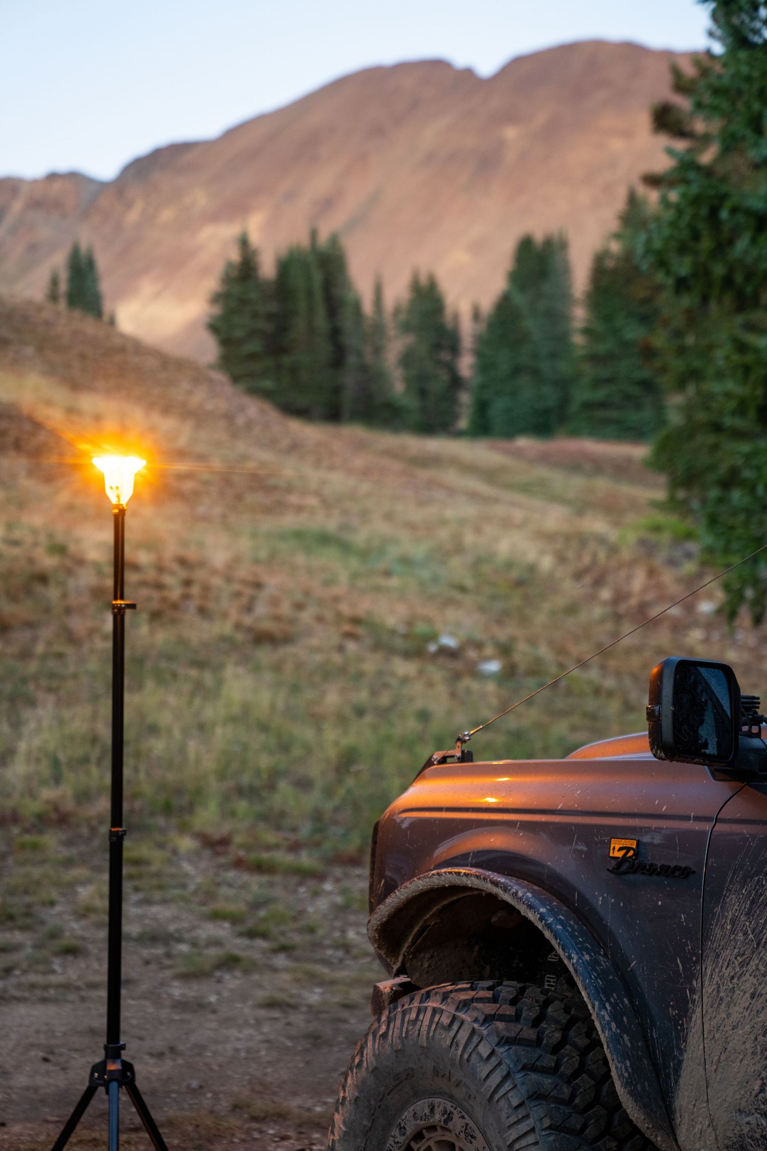 Off-road vehicle parked near illuminated lamp post against rugged mountain backdrop at dusk.