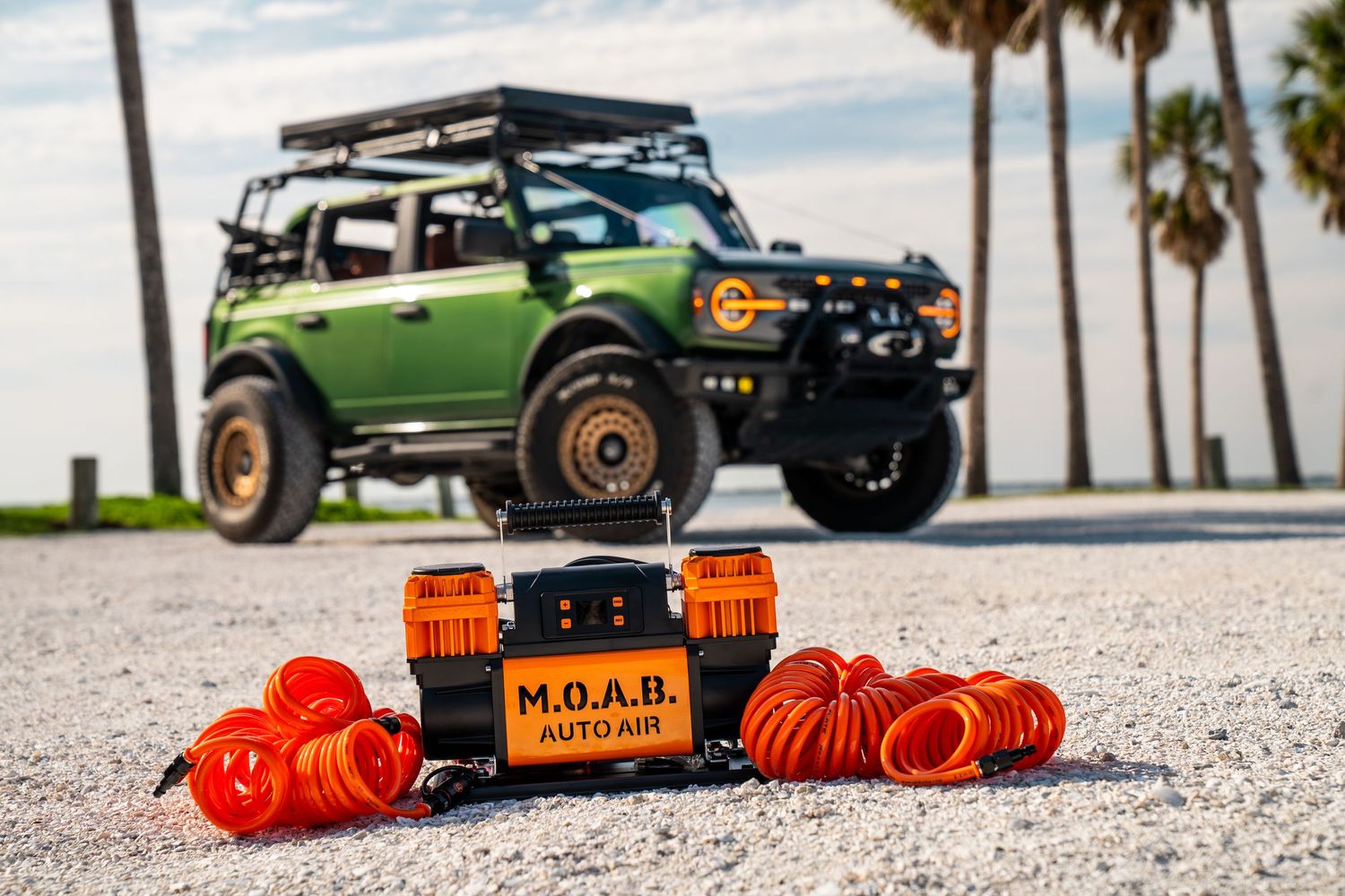 Green Ford Bronco with roof rack parked on beach with orange recovery boards displayed in foreground.