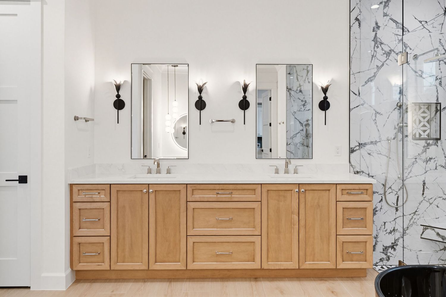 Modern bathroom vanity with light wood cabinets, dual sinks, black sconces and marble accent wall.