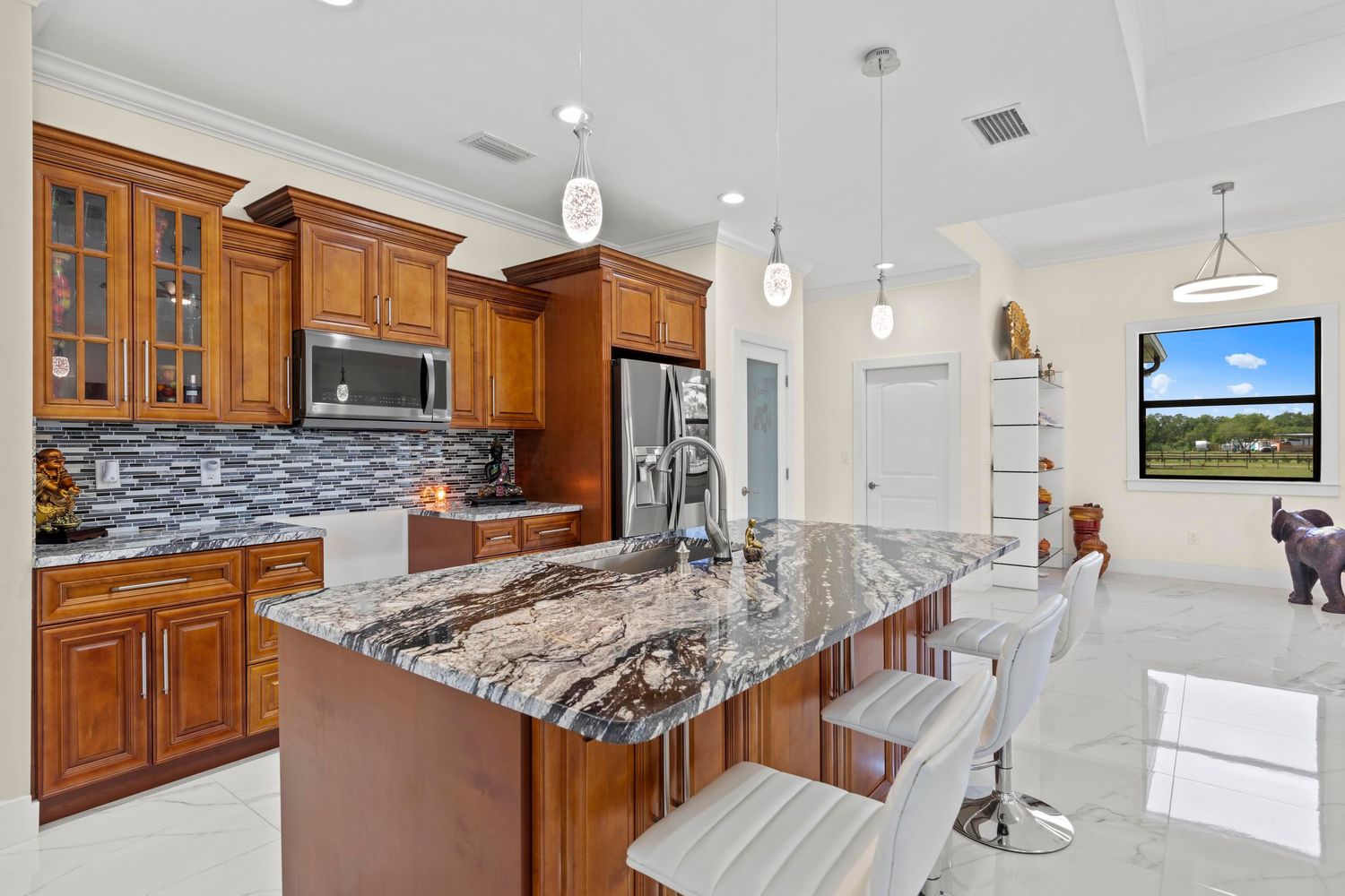 Modern kitchen interior with white marble countertops, wood cabinets, pendant lights and stainless steel appliances.