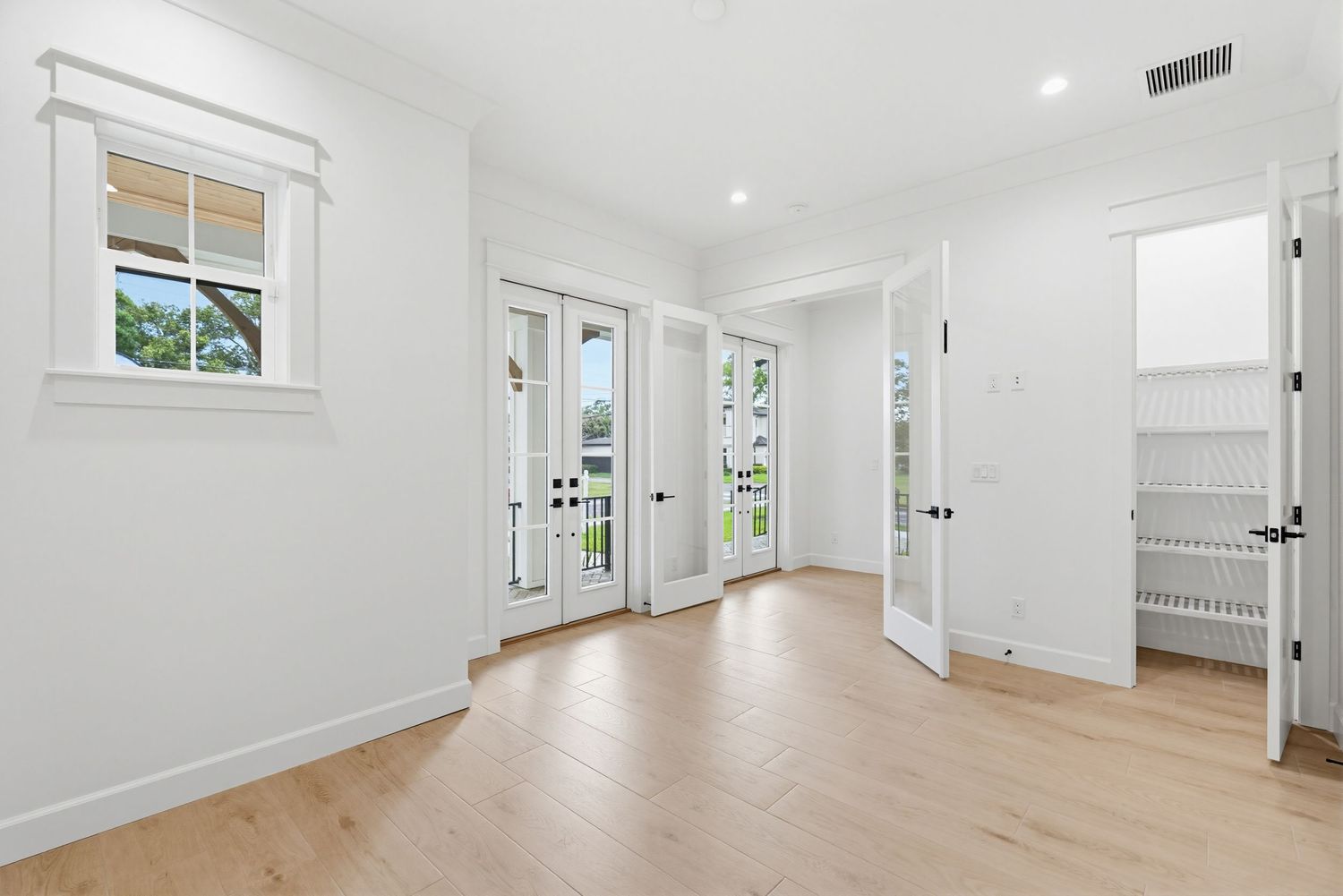 Modern white hallway with light hardwood floors, recessed lighting, and multiple doorways leading to different rooms.