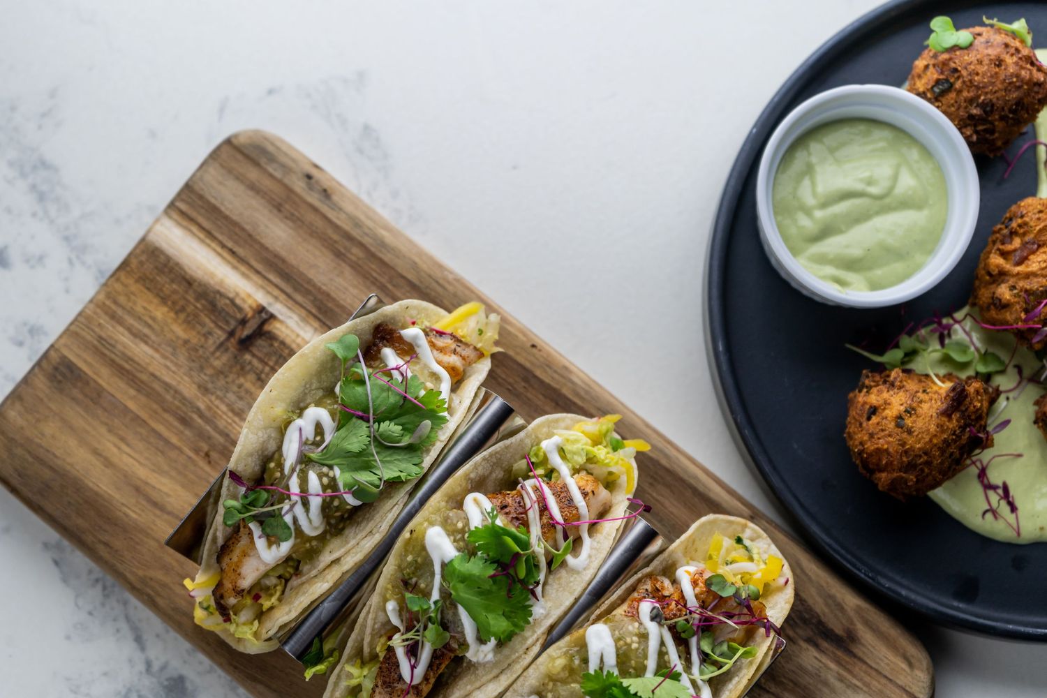 Fresh fish tacos topped with cabbage slaw, cilantro, and creamy sauce served on wooden boards and dark plates.