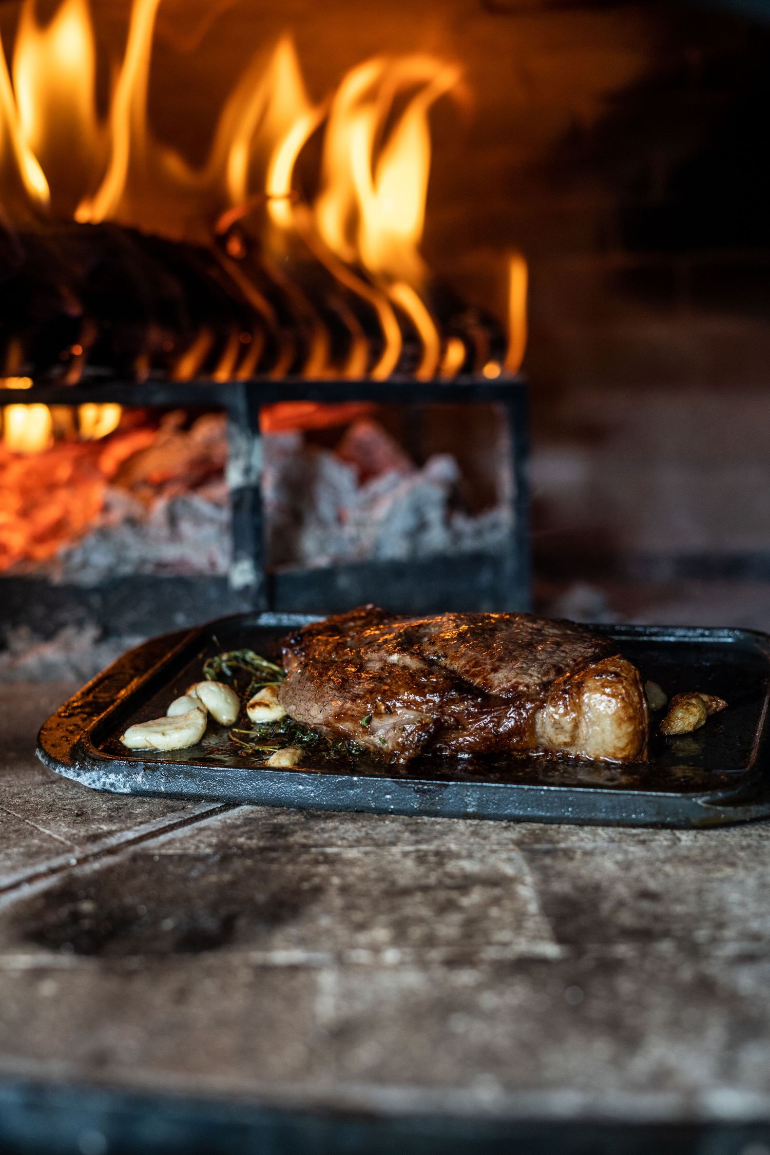 Close-up shots of meat grilling over flames on a flat top grill surface.