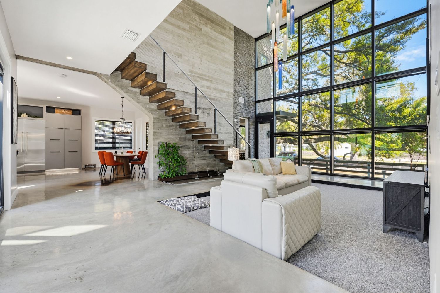Modern staircase with glass railings and stone steps leads upward in a contemporary home with large windows.