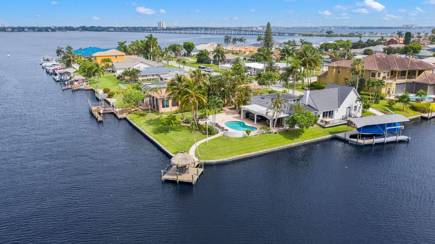 Aerial panoramic view of waterfront homes and docks along a Florida canal with boats and palm trees.