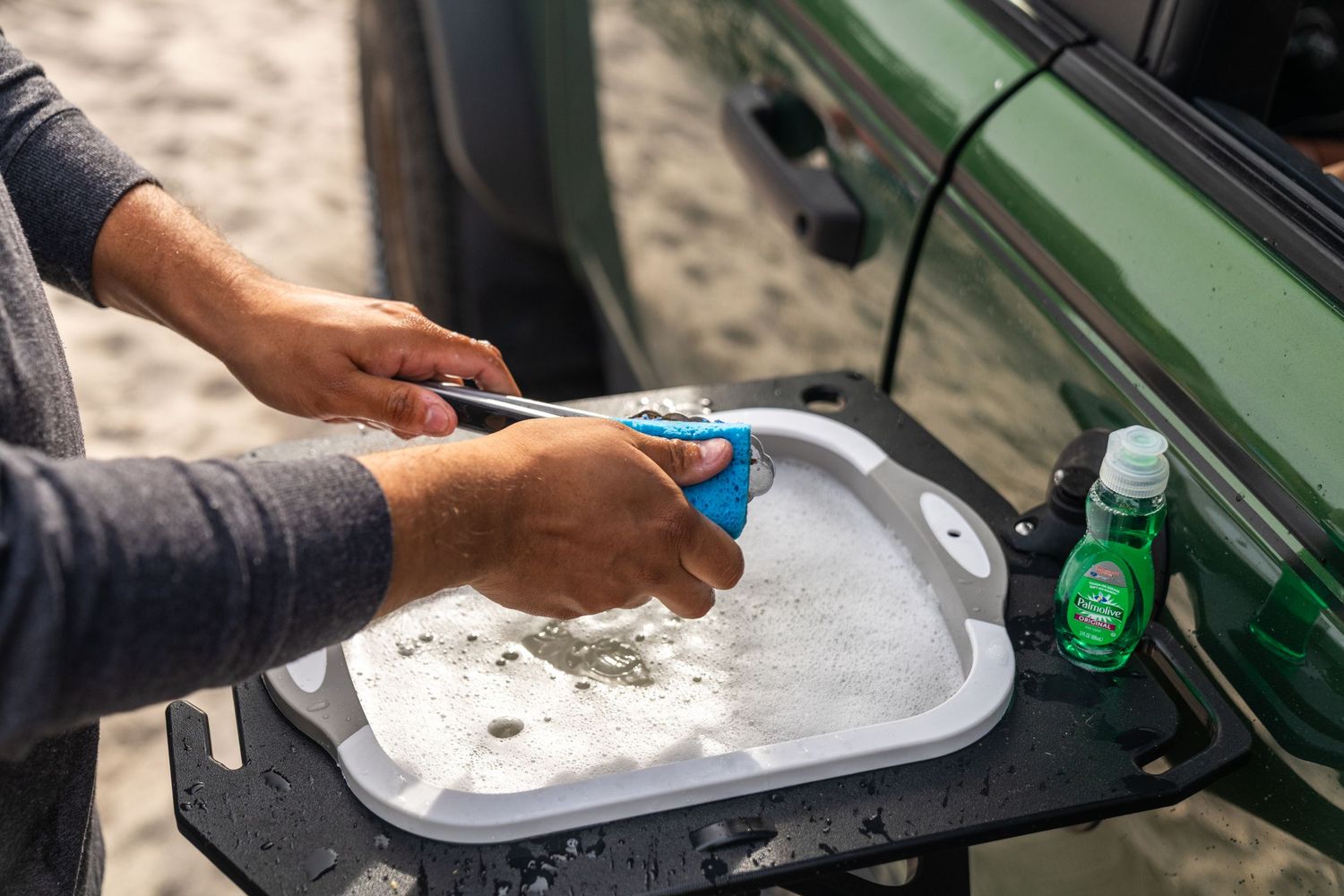 Hands preparing food on a fold-out table attached to a green Ford Bronco.