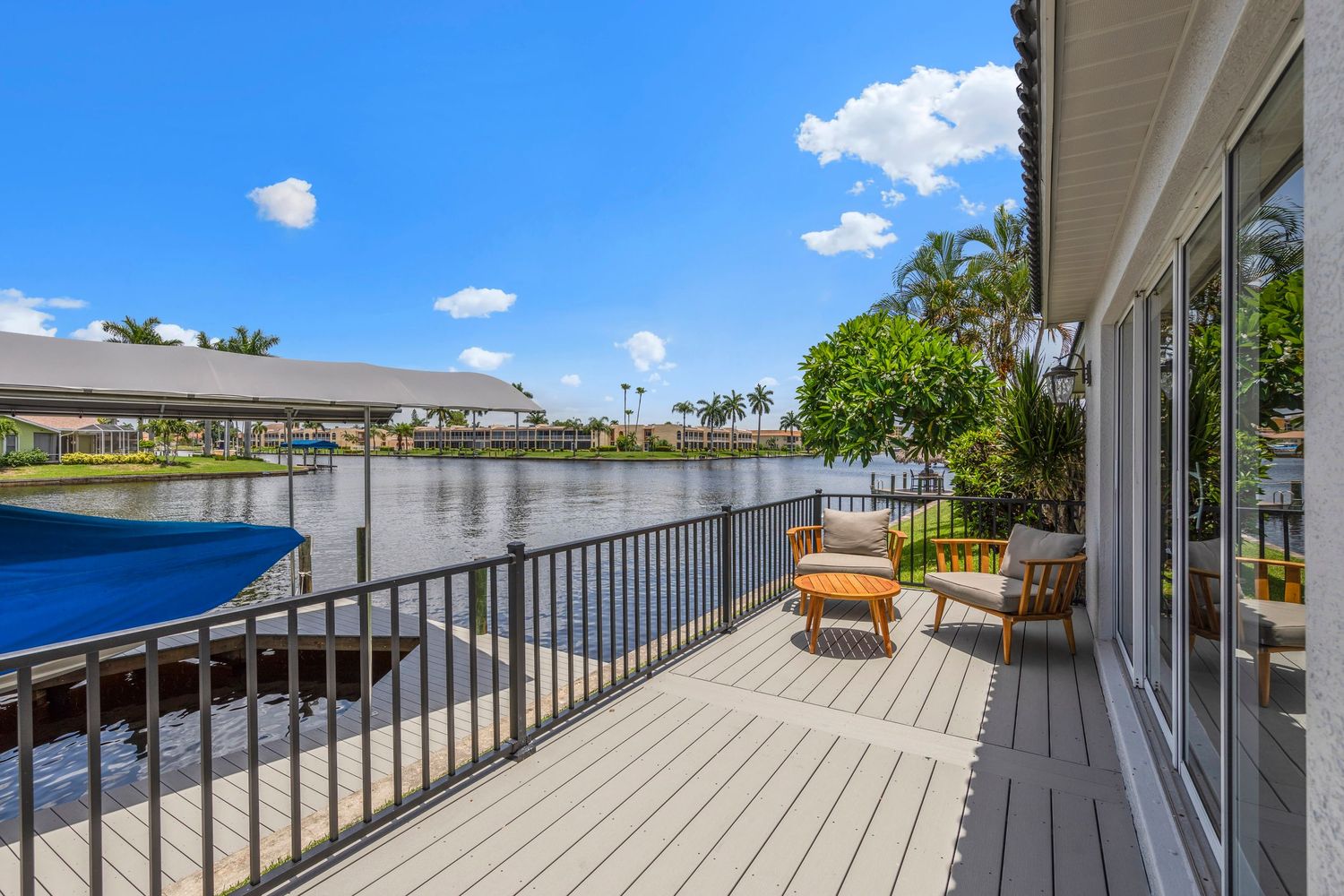 Panoramic view of a spacious white deck with railing overlooking palm trees and blue sky on a sunny day.