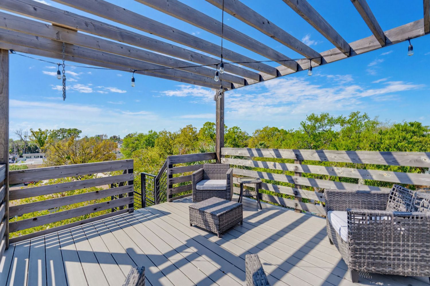Modern rooftop deck with wooden pergola and gray outdoor furniture overlooking a sunny cityscape view.