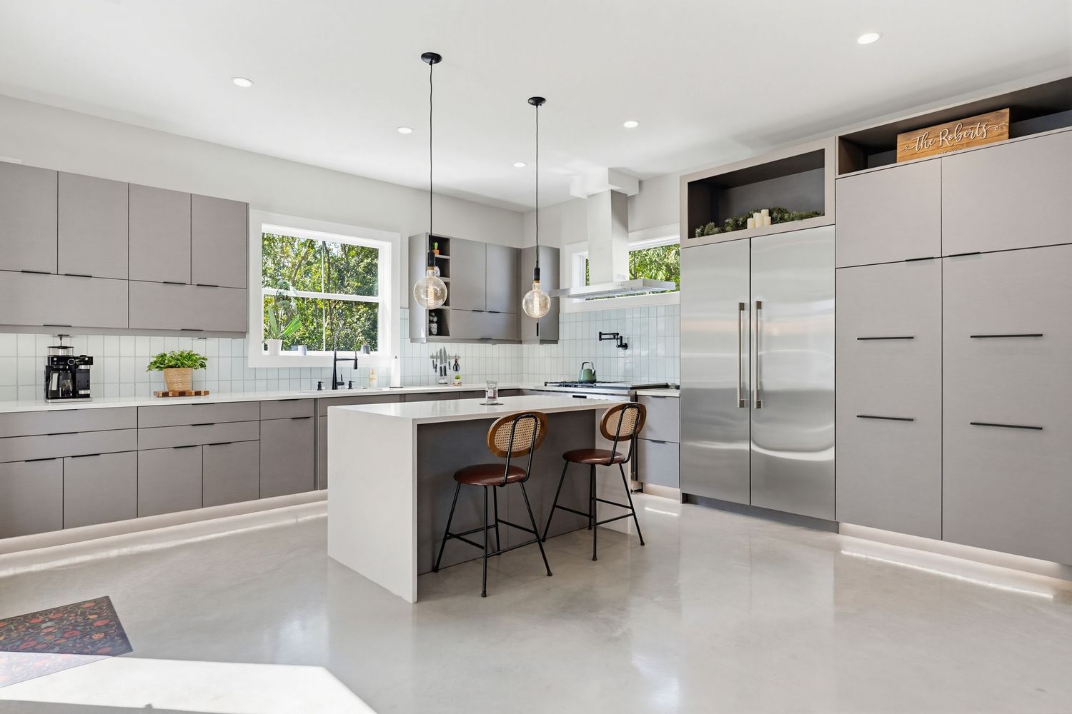 Modern open concept kitchen with gray cabinets, white countertops, and pendant lighting in a bright minimalist space.