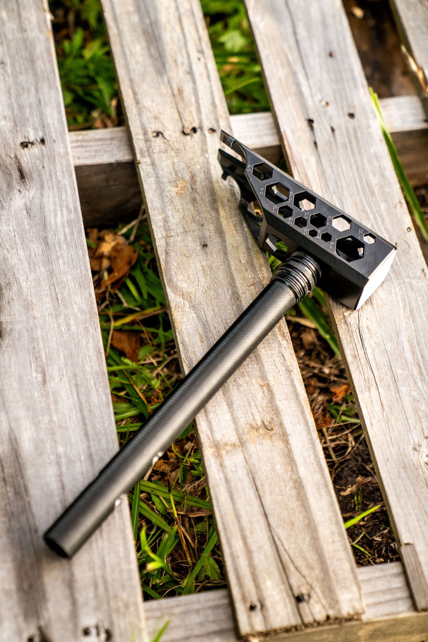Black metal tool with hexagonal cutouts resting on weathered wooden fence slats.