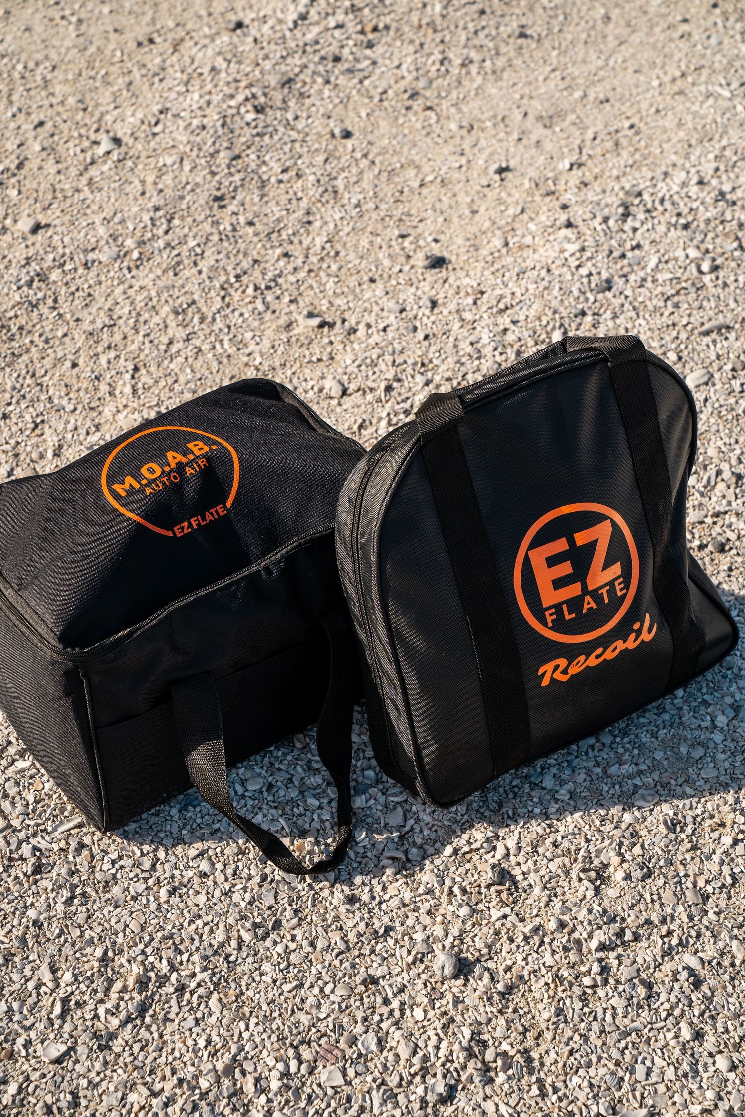 Row of black gear bags with orange EZ Racing logos laid out on gravel surface.