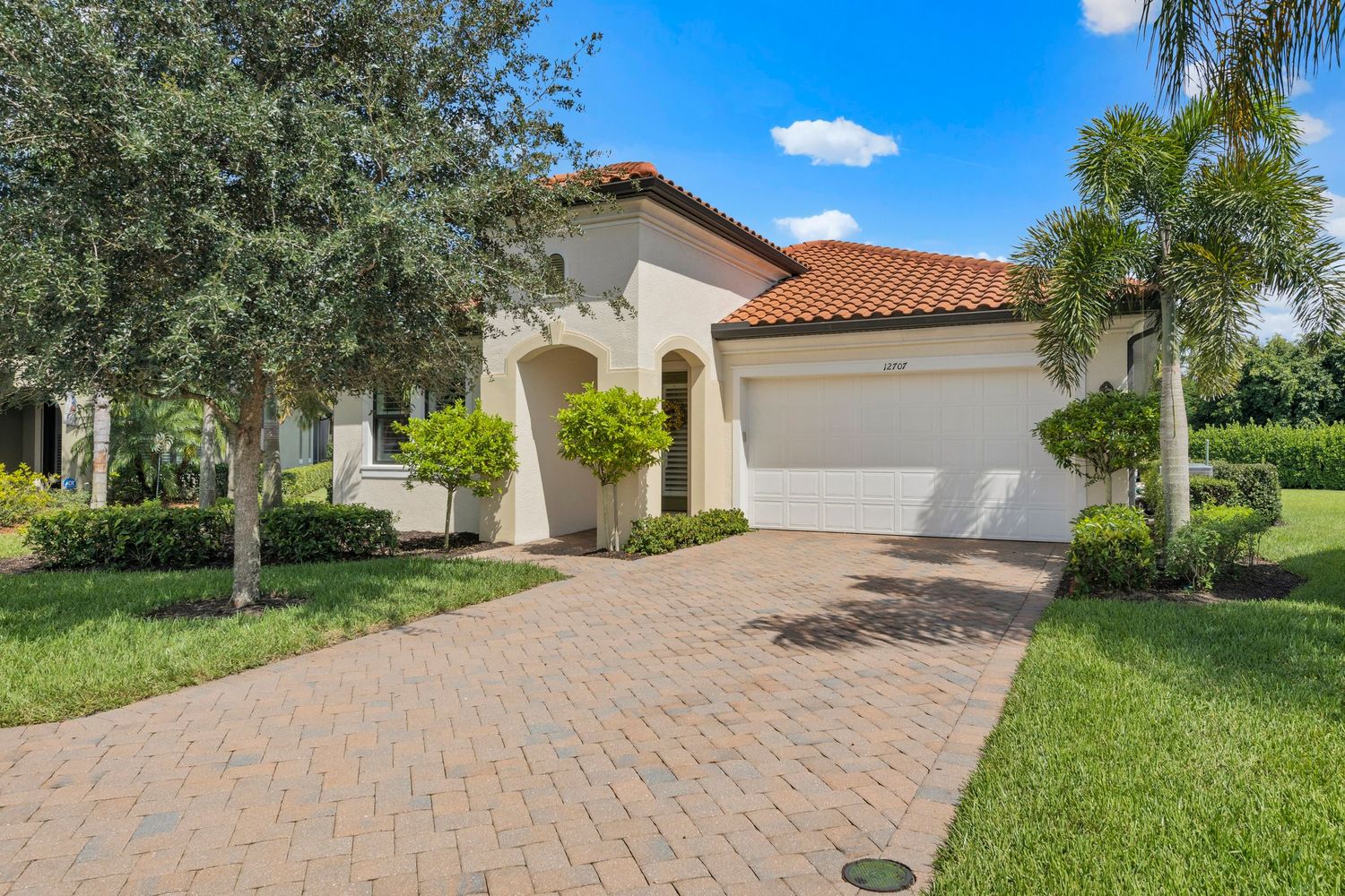 Curved brick paver driveway leading to Mediterranean style home with palm trees and manicured landscaping.