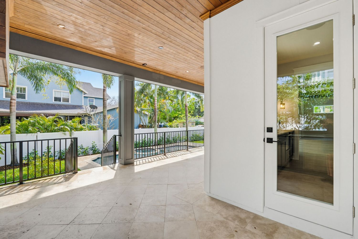 Modern covered patio with wood ceiling and white columns overlooks a landscaped backyard with palm trees.