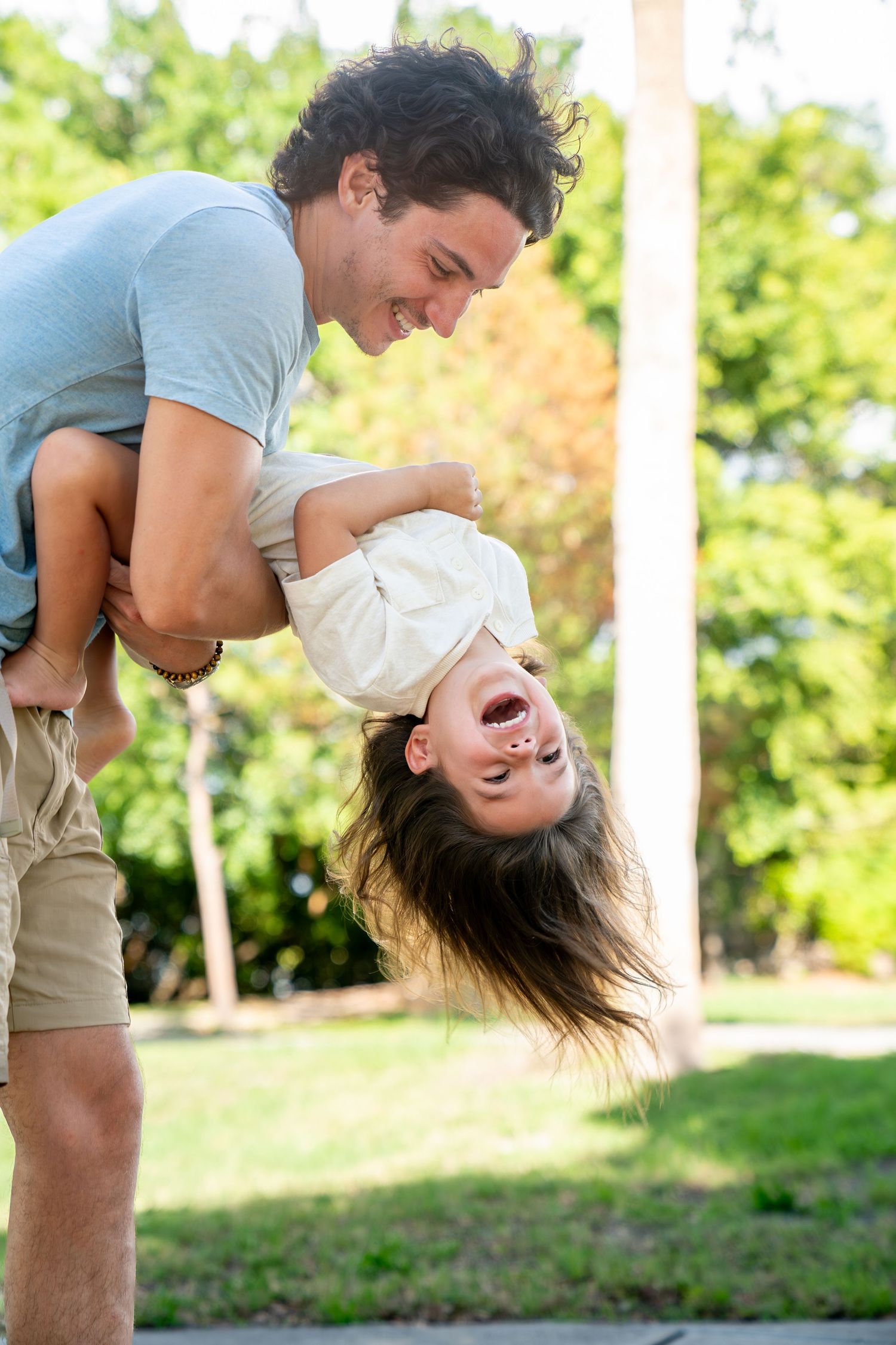 A playful couple shares a tender moment in a park setting with green trees and grass in the background.