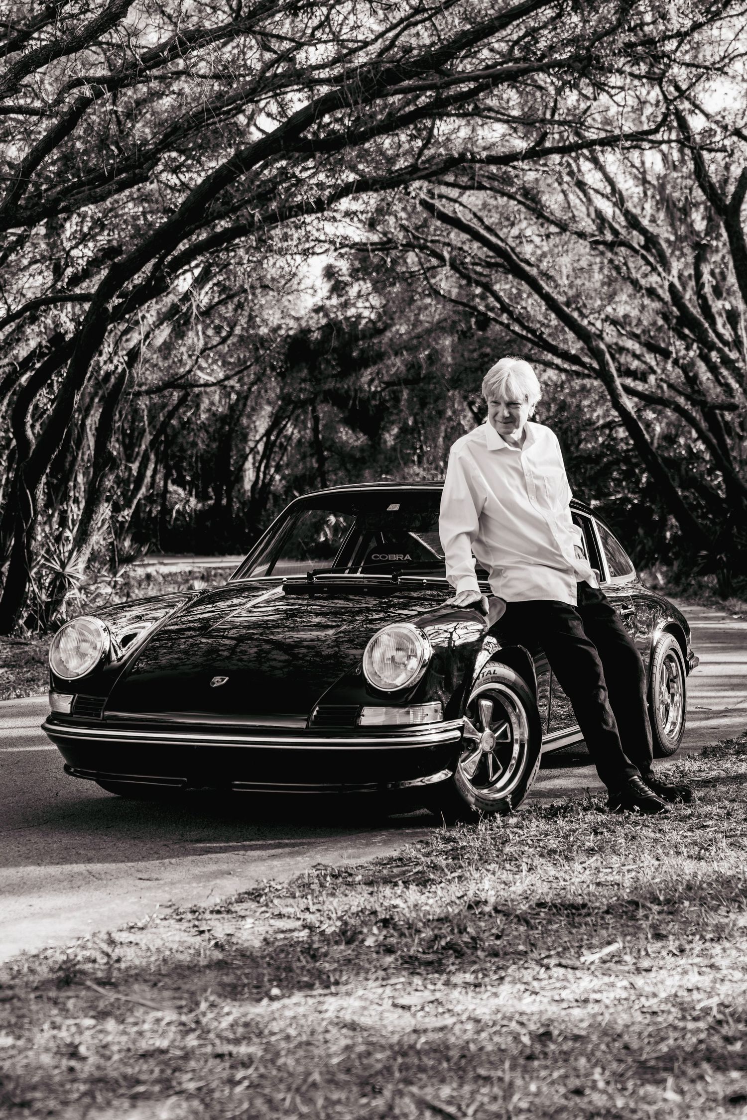 Black and white photo series showing a classic car parked under arching tree branches in a moody outdoor setting.