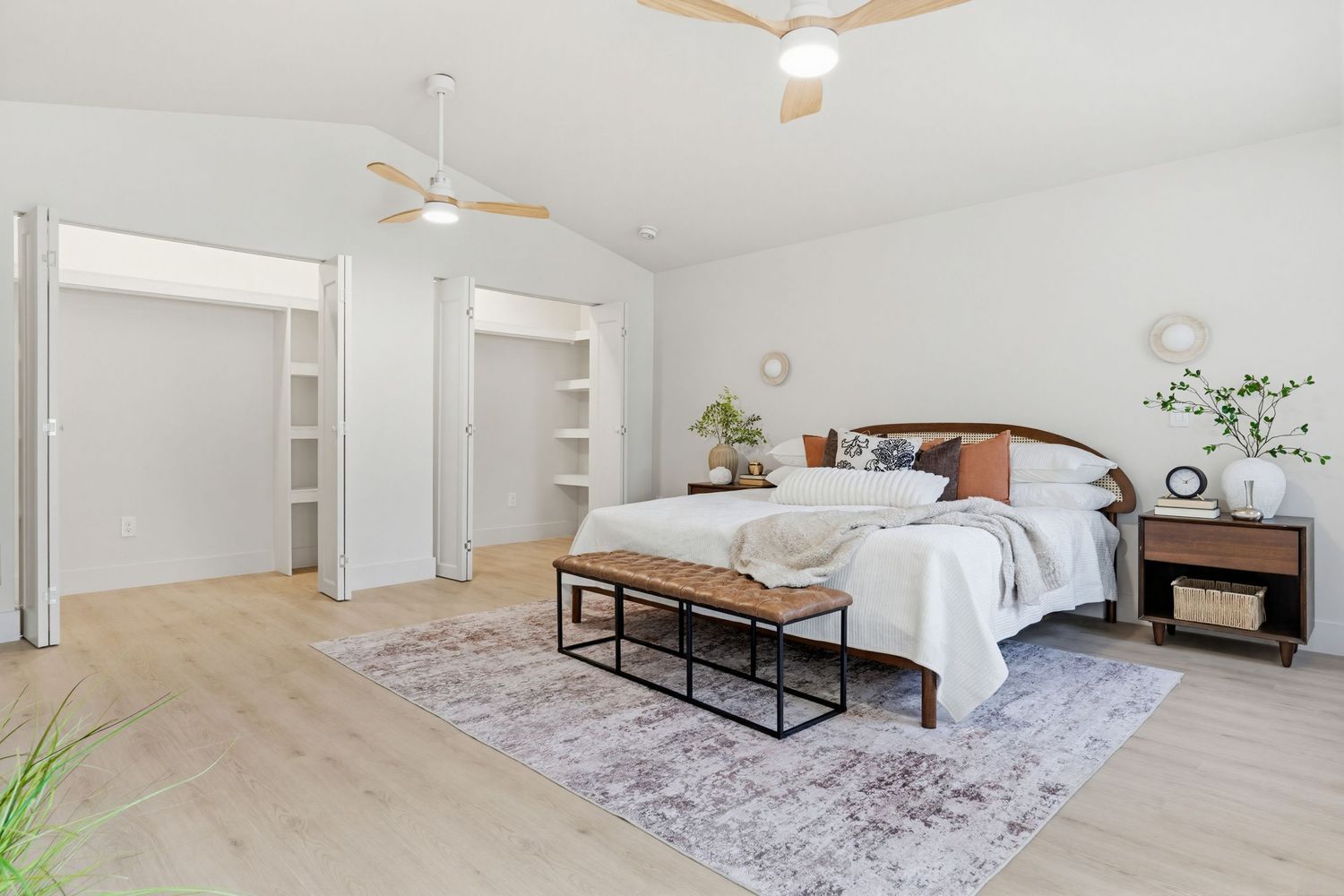 Modern minimalist bedroom with white bedding, ceiling fan, and light gray area rug in a bright sunlit space.