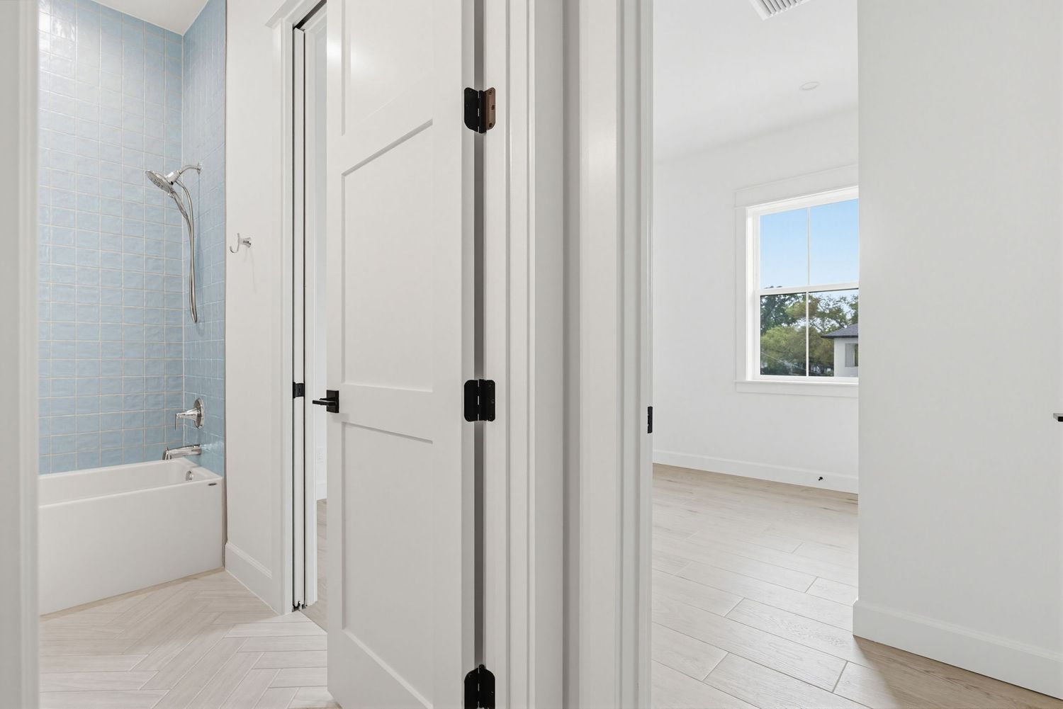 Modern white hallway with bathroom entrance and window showing bright interior design details.