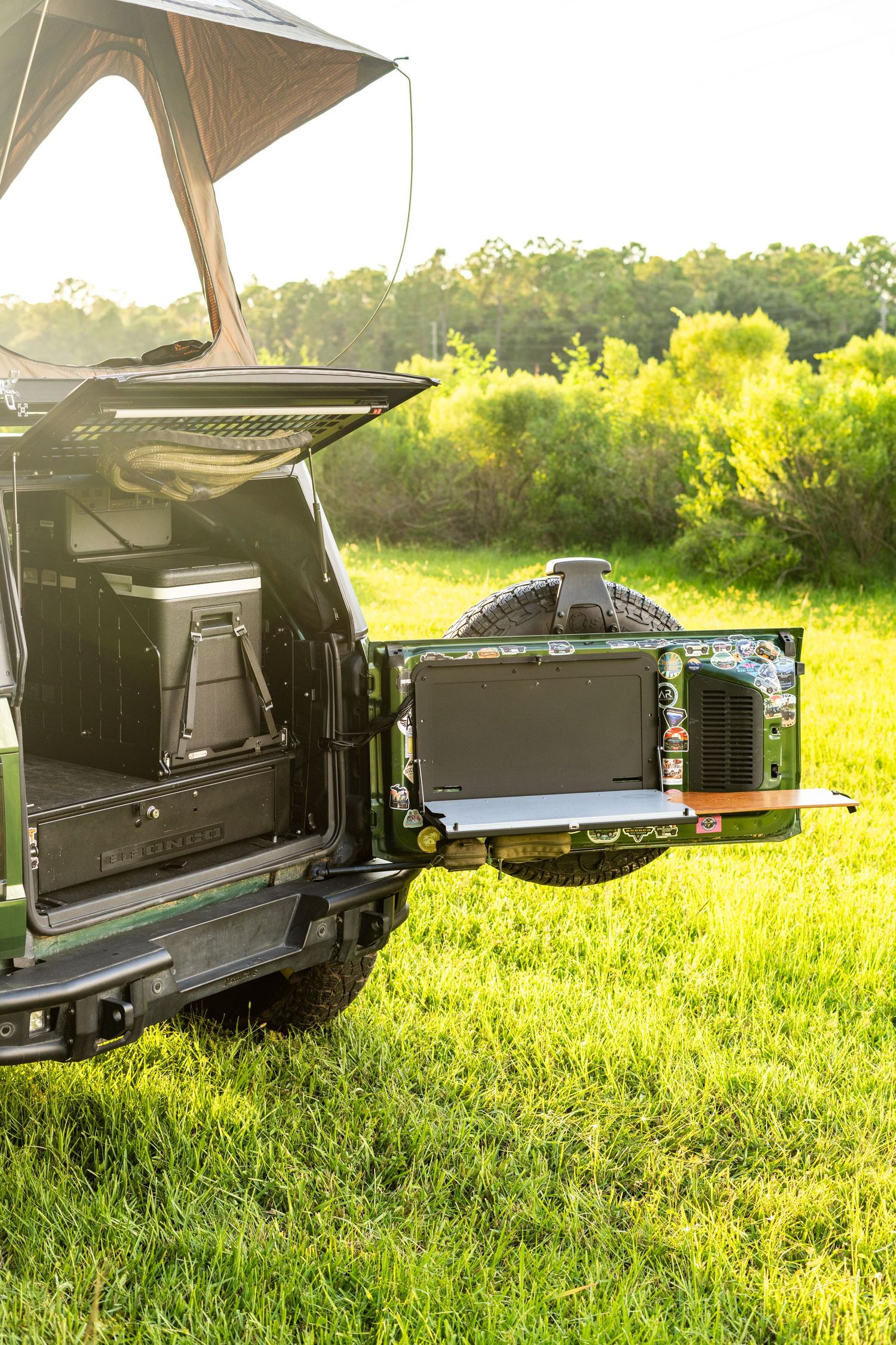 Vehicle camping setup with awning and electronic equipment displayed in grassy field at sunset.