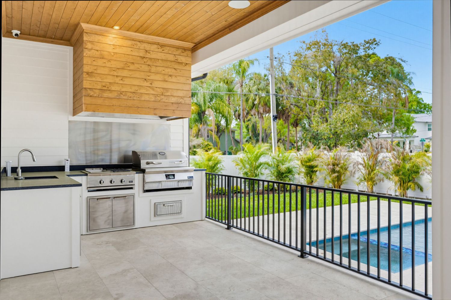 Modern outdoor kitchen and entertaining area with wood ceiling and pool view showcases sleek stainless steel appliances.
