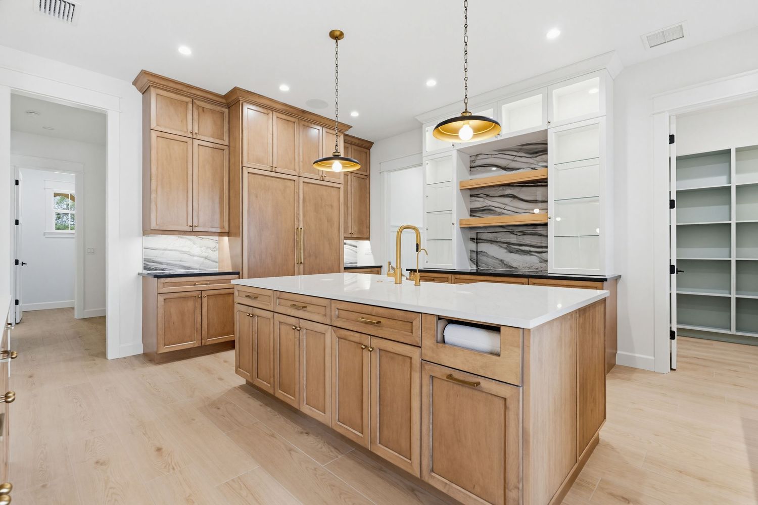 Modern kitchen with light wood cabinets, white quartz countertops, and pendant lighting in an open-concept layout.