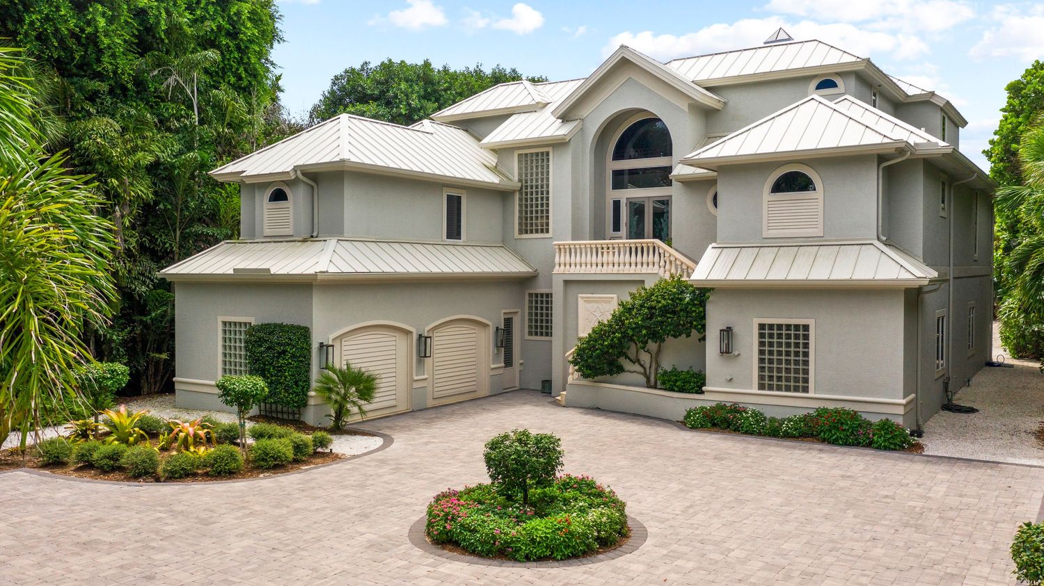 Panoramic view of a modern white luxury home with tropical landscaping and circular driveway in Florida.