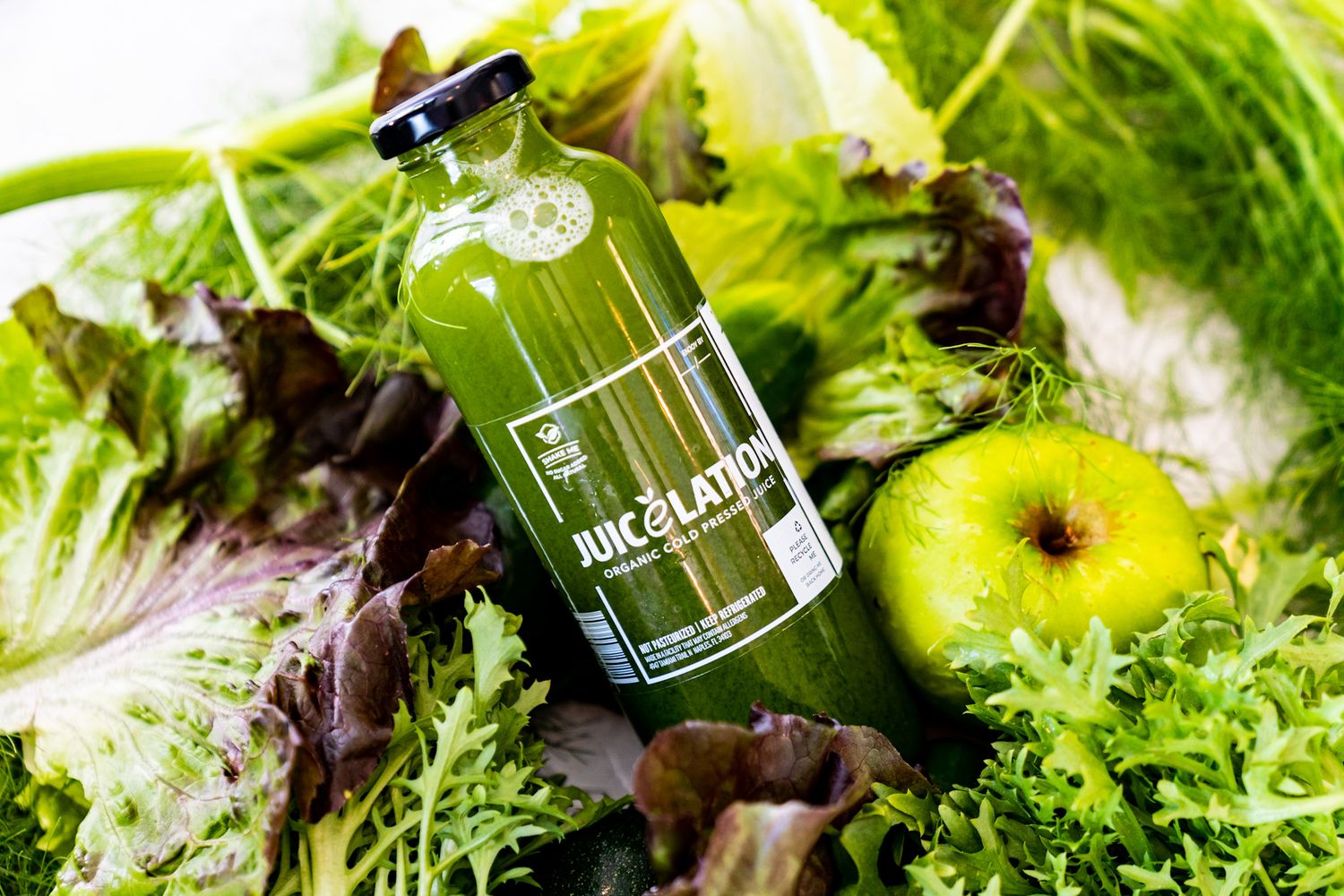 Fresh mixed green salad leaves with yellow flowers and olive oil being drizzled from a glass bottle.