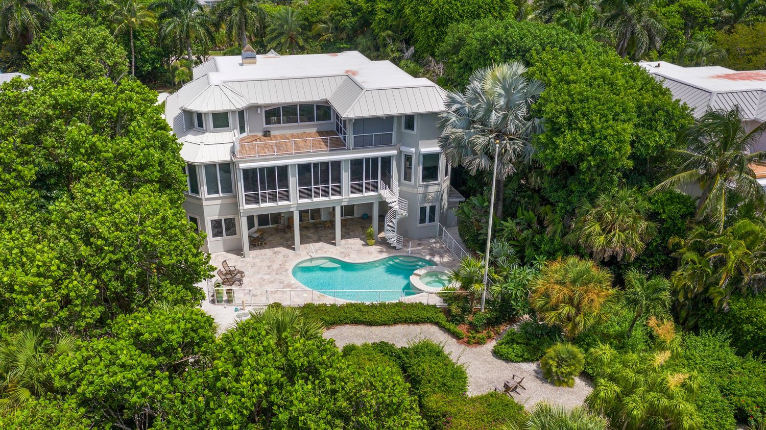 Aerial panoramic view of a modern white waterfront home with pool surrounded by lush tropical landscaping.