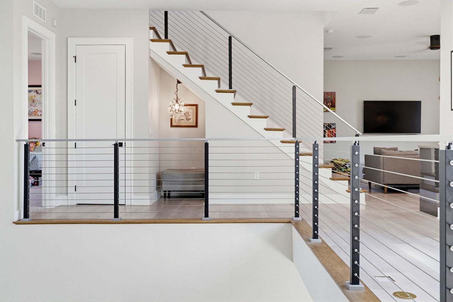 Modern interior staircase with horizontal metal railings and wooden steps in a bright white living space.