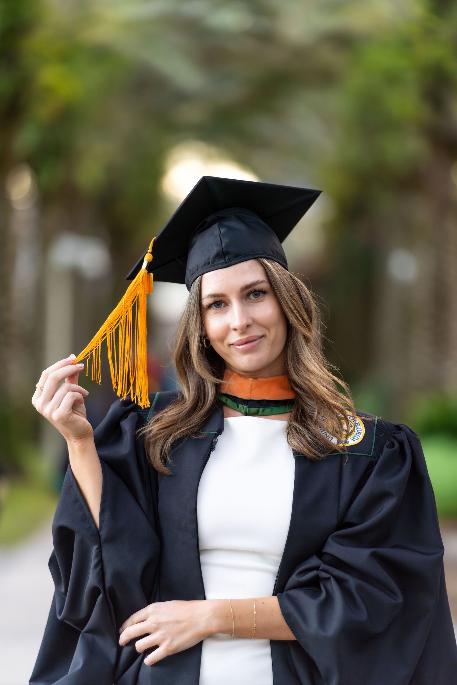 A graduate in black cap and gown holds and plays with the yellow tassel during outdoor graduation photo session.