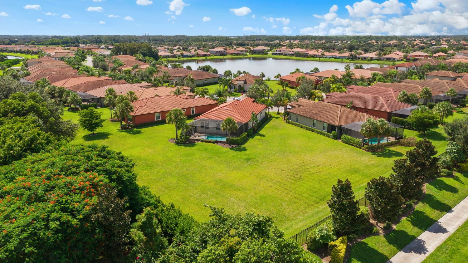 Aerial panoramic view of luxury residential homes with lush green lawns and landscaping in a Florida neighborhood.