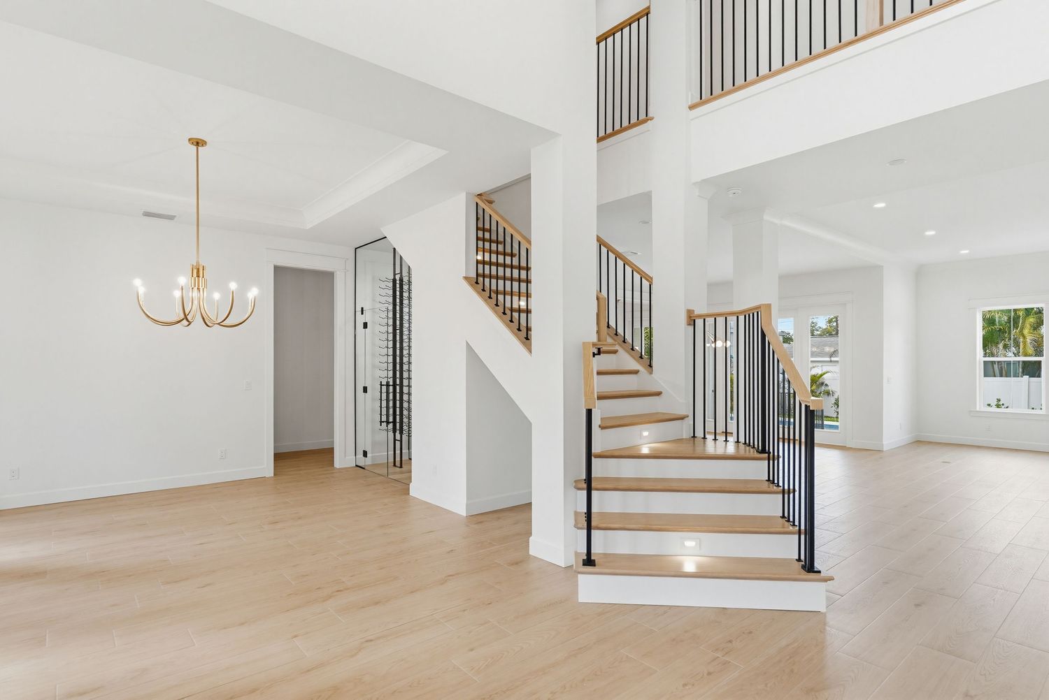 Modern white staircase with wooden treads and black metal railings in an open concept living space.