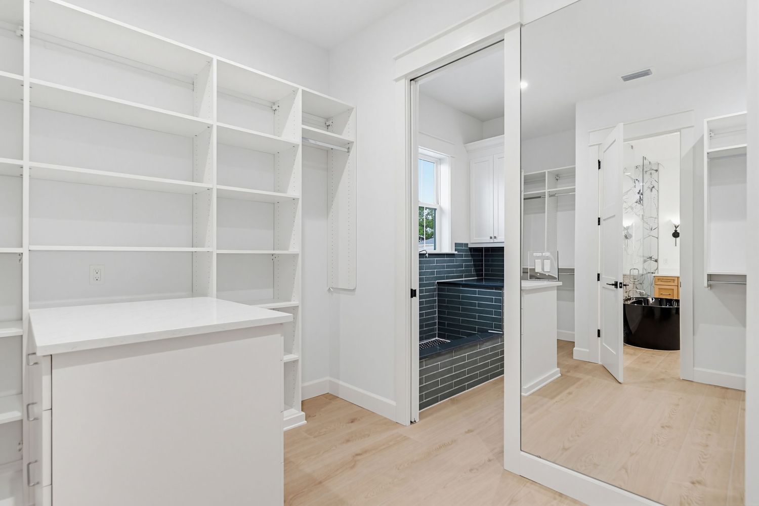 Modern walk-in closet with white built-in shelves, mirrored sliding doors and light hardwood flooring.