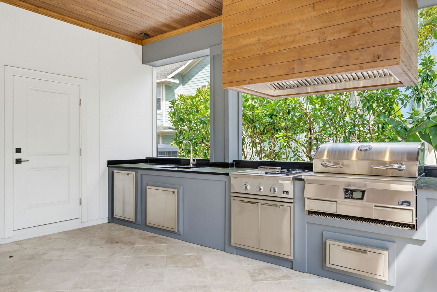 Modern outdoor kitchen with wood plank ceiling, stainless steel appliances, and white cabinets under covered patio.