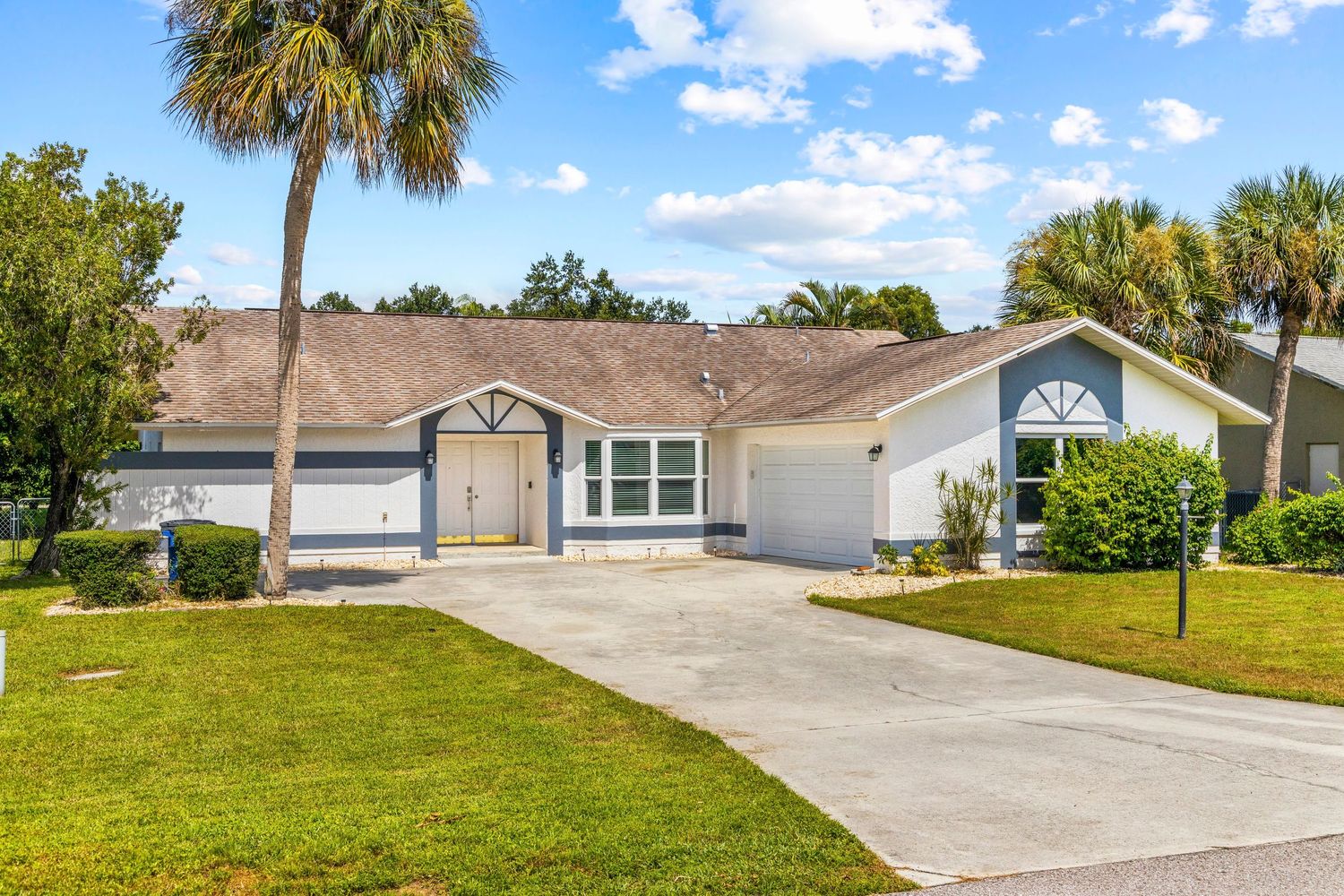 Panoramic view of a single-story beige ranch house with palm trees and a concrete driveway in Florida.