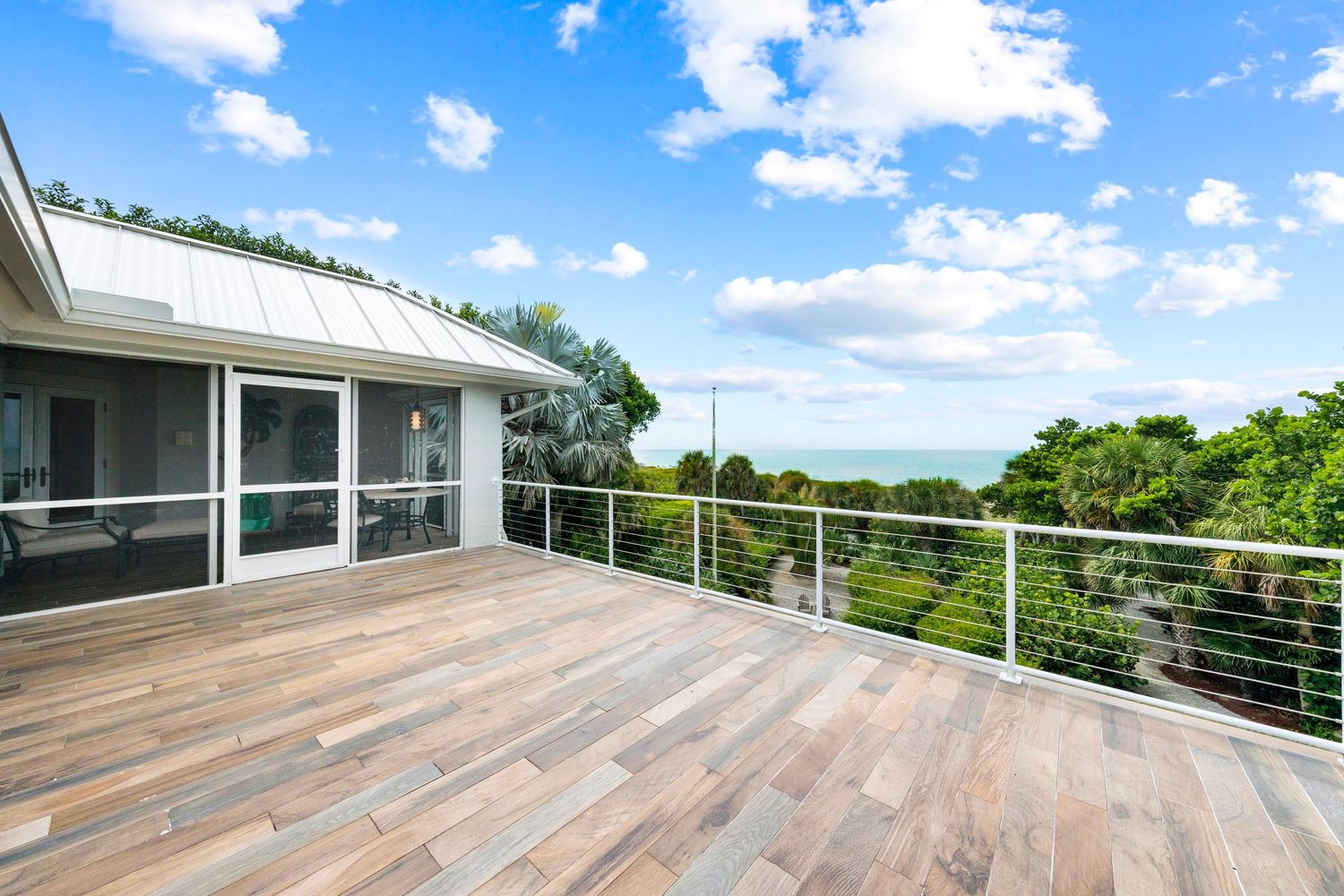 Modern wooden deck with metal railings overlooking lush tropical landscape and blue sky on sunny day.