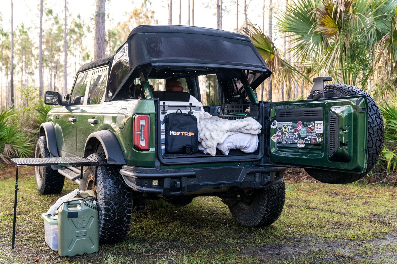 Green off-road vehicles parked in a wooded area with palm trees.