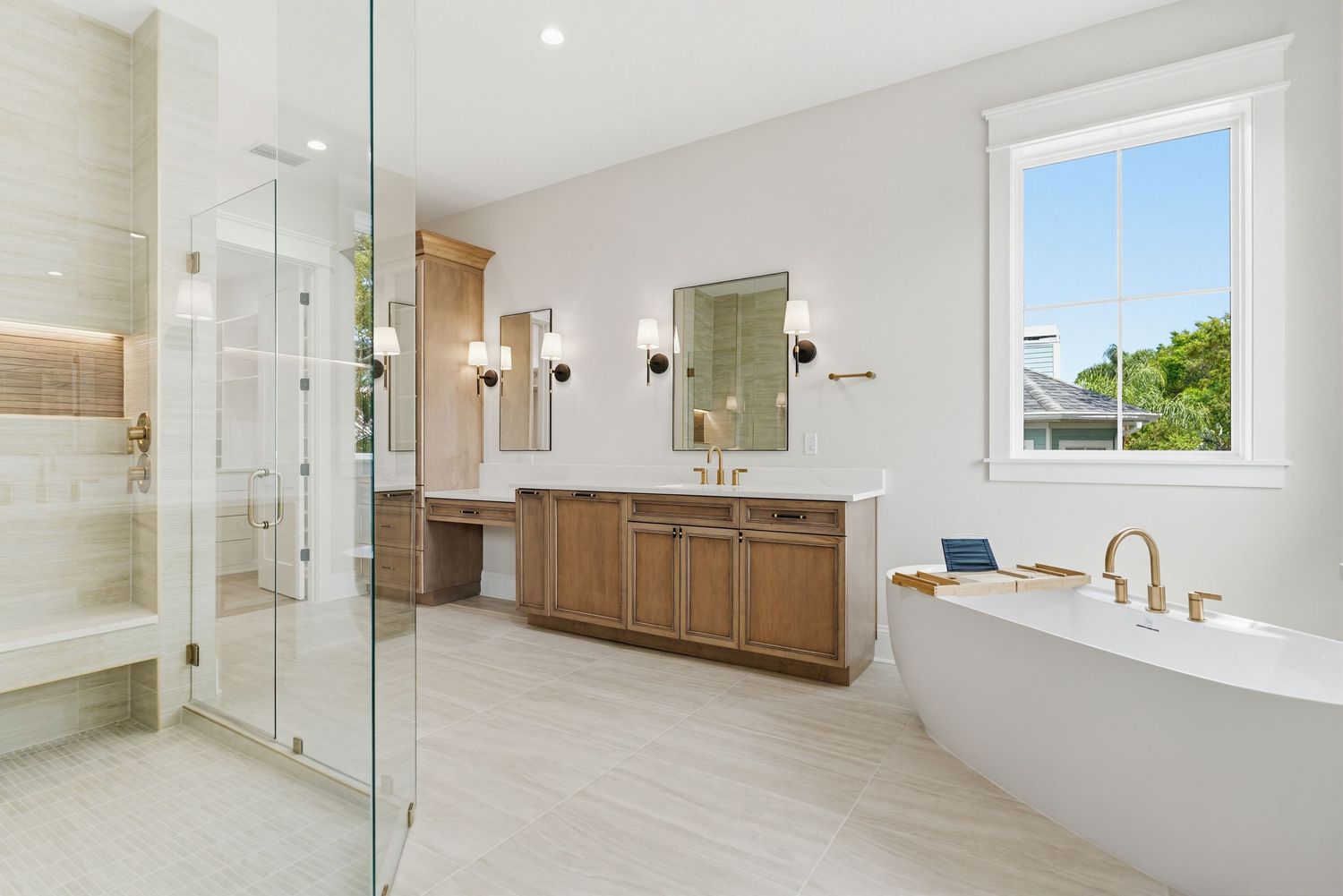 Modern luxury bathroom with freestanding tub, glass shower enclosure, and wooden vanity featuring gold fixtures.