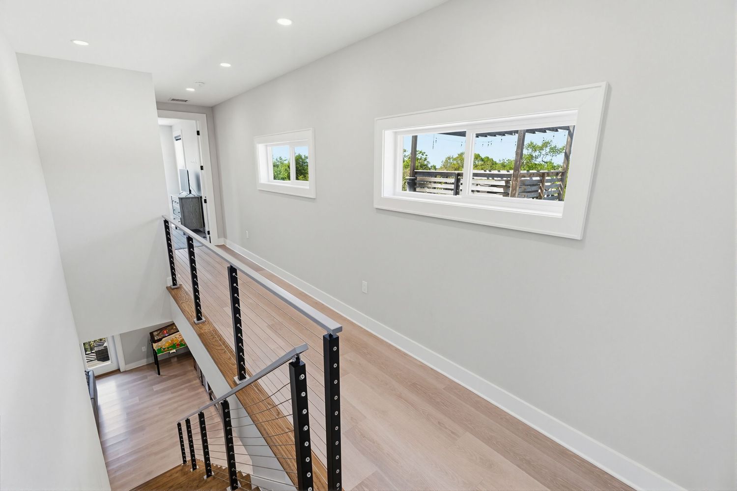 Modern white staircase with black metal railings and light hardwood steps leads to upper level with bright windows.