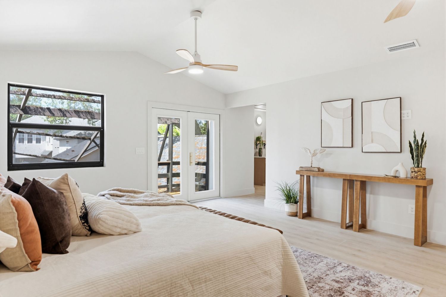 Modern white bedroom with wood accents features a ceiling fan, plush bedding, and minimalist decor on the walls.
